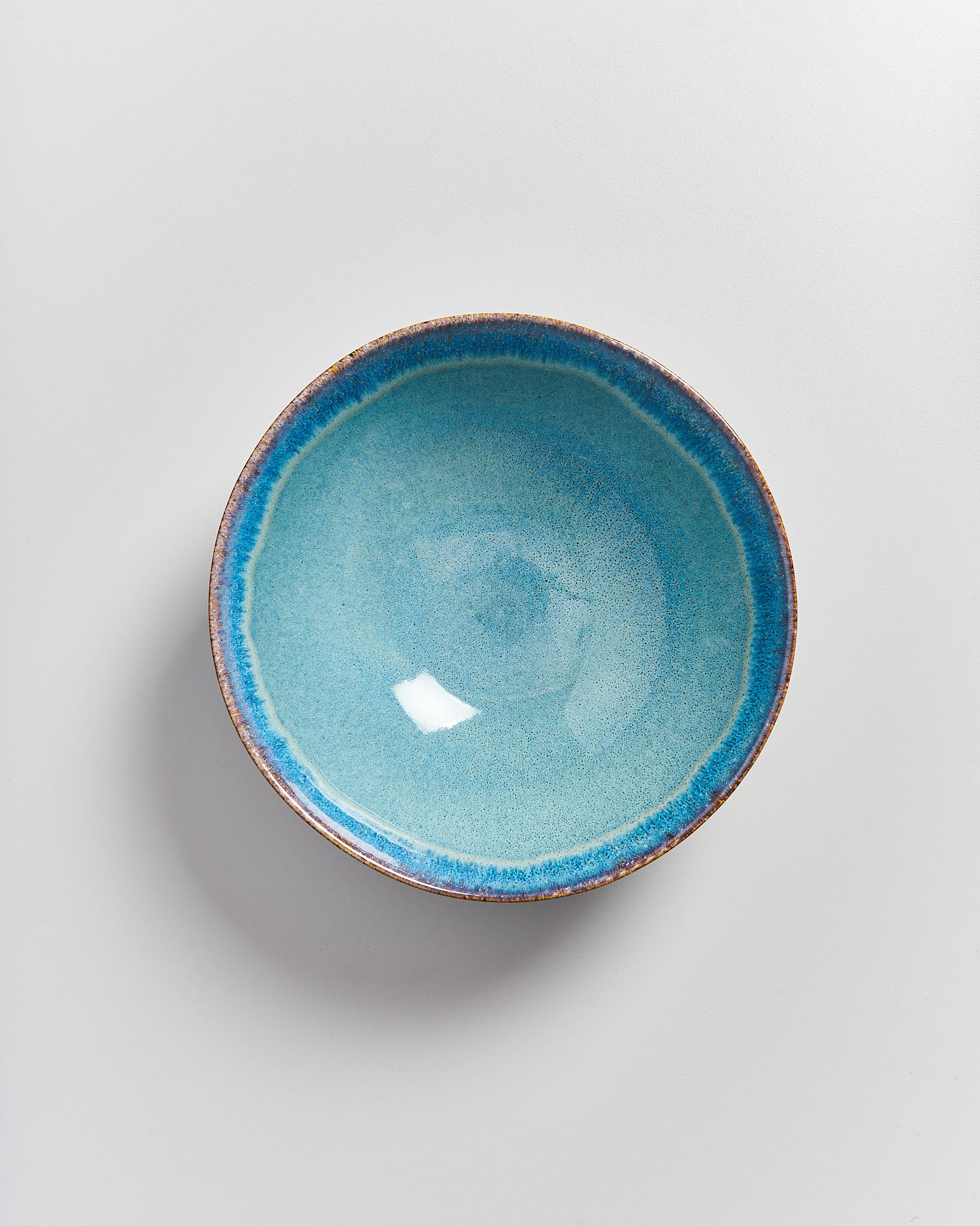 Eine einzelne blau glasierte Keramikschale auf einem hellen Hintergrund.