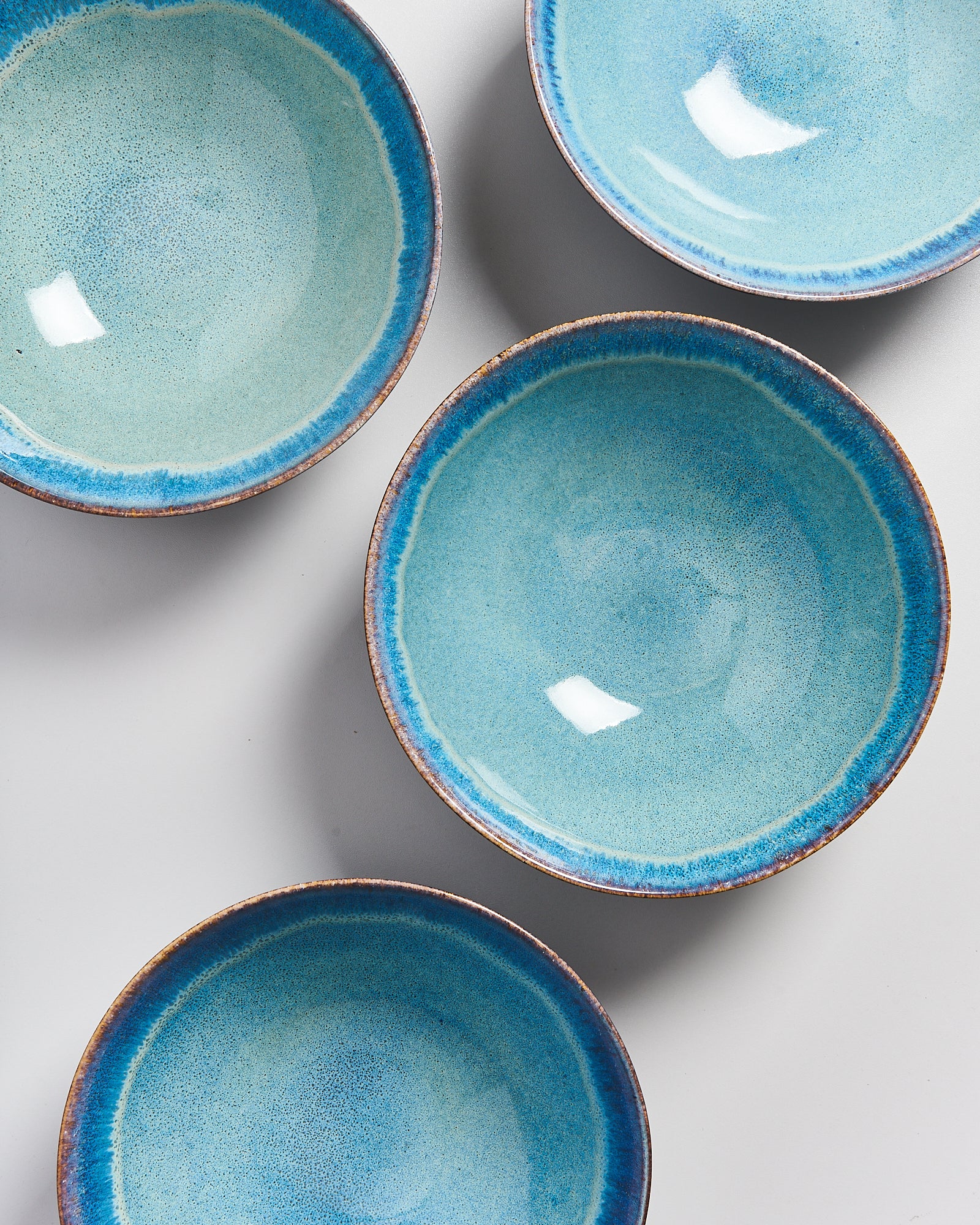 Vier türkisfarbene Keramikschalen mit dunkelblauem Rand auf einer grauen Oberfläche.