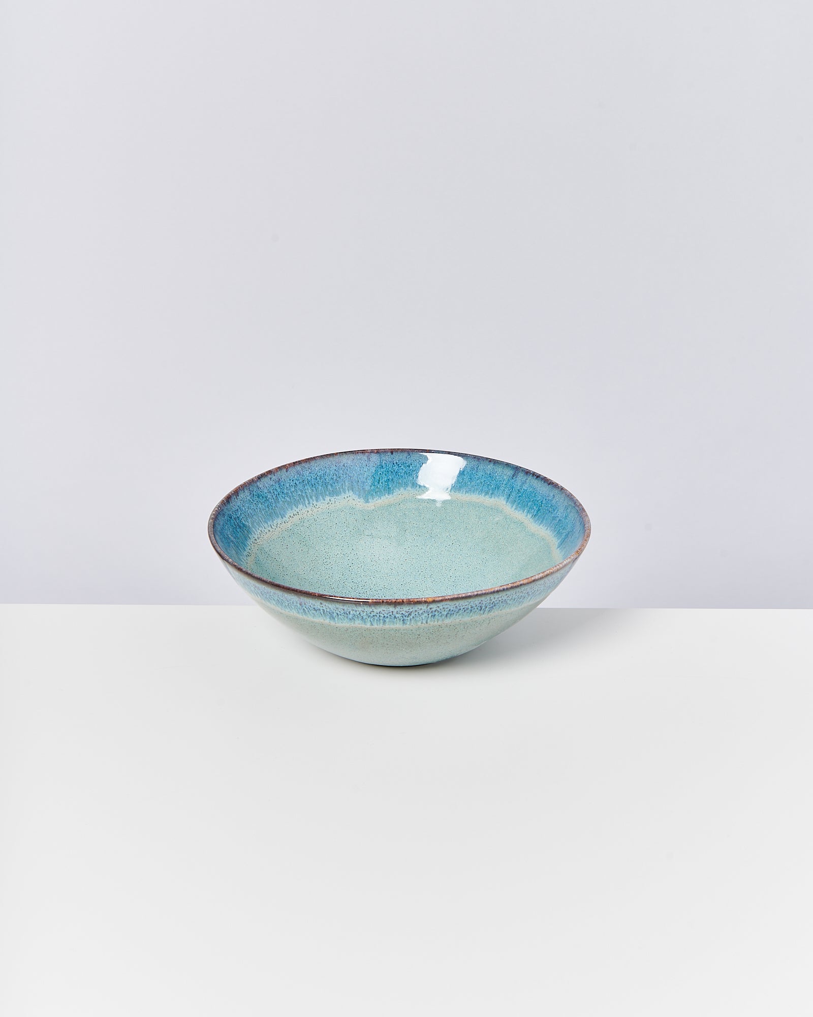 Keramikschale mit blau-grüner Glasur auf weißem Hintergrund.