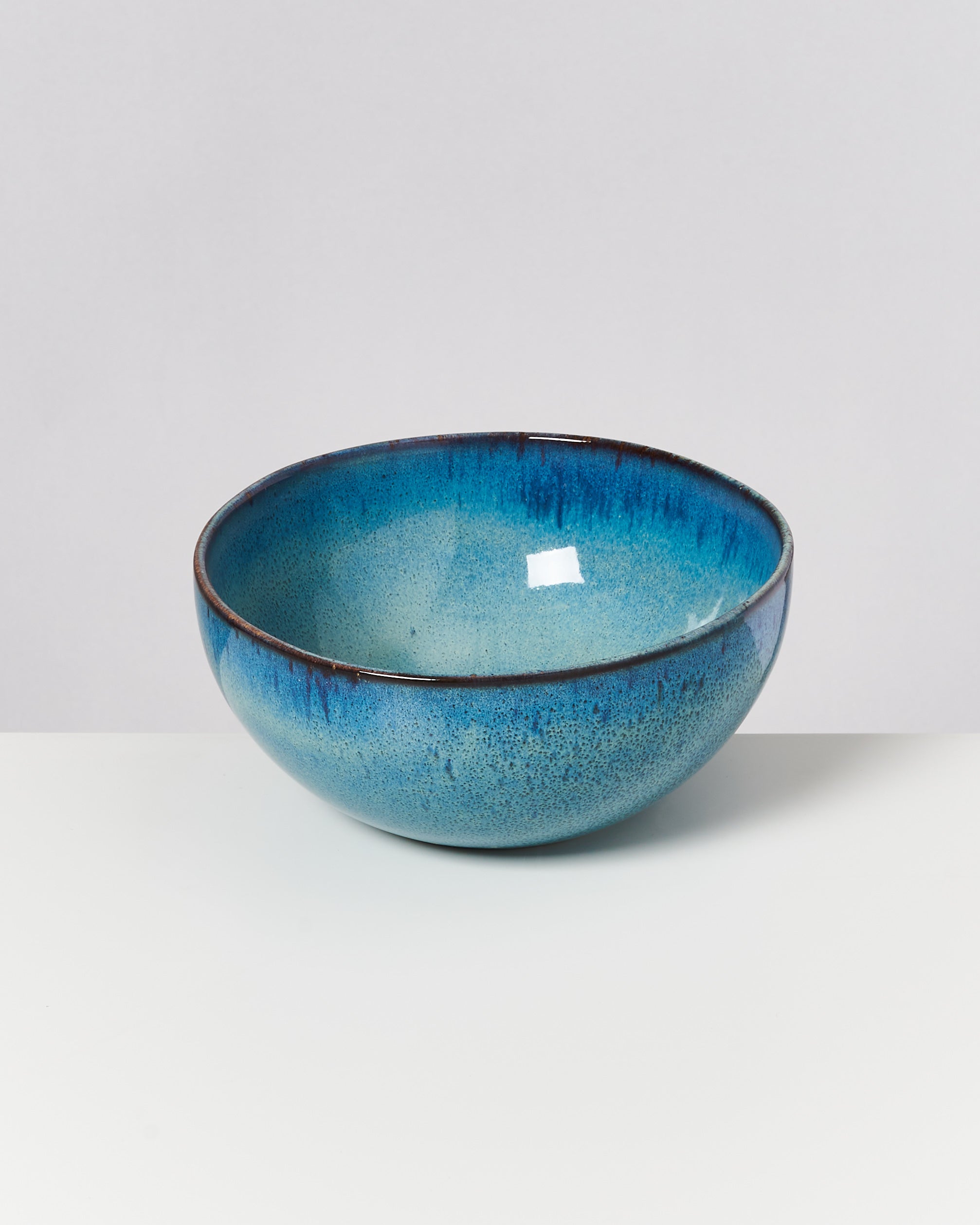 Eine blau glasierte Schüssel mit dunklen Rändern auf einer weißen Oberfläche vor grauem Hintergrund.
