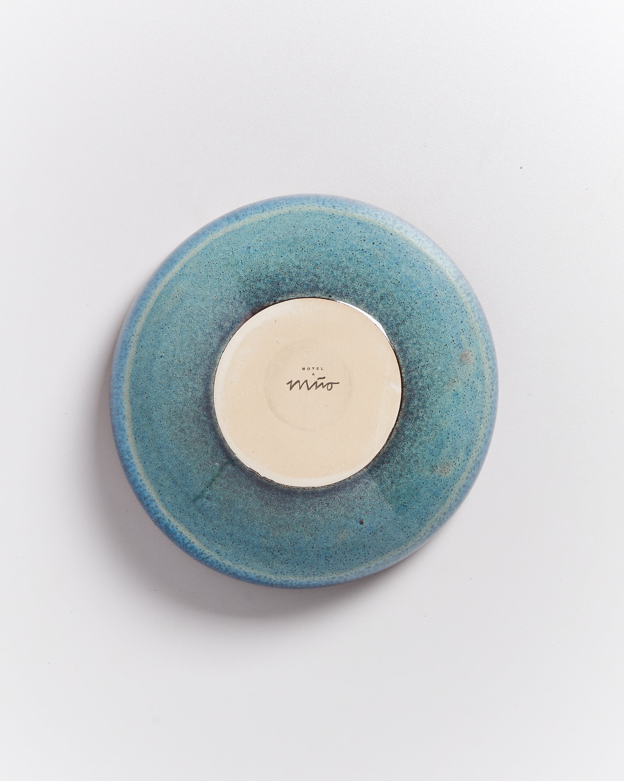 Rückseite eines blaugrünen Keramiktellers mit einem weißen Kreis in der Mitte, auf dem "Hotel Mito" steht.