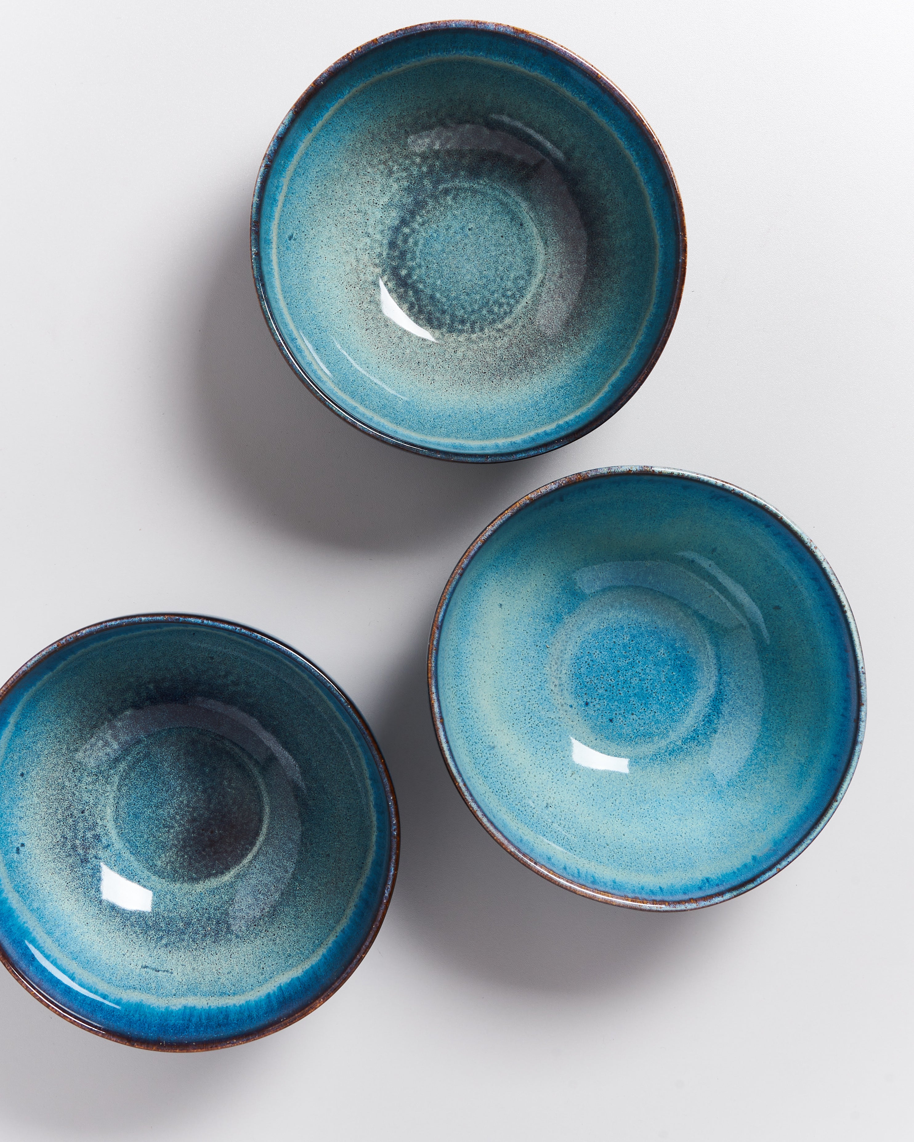 Drei blaue, glasierte Keramikschalen liegen auf einem weißen Hintergrund.