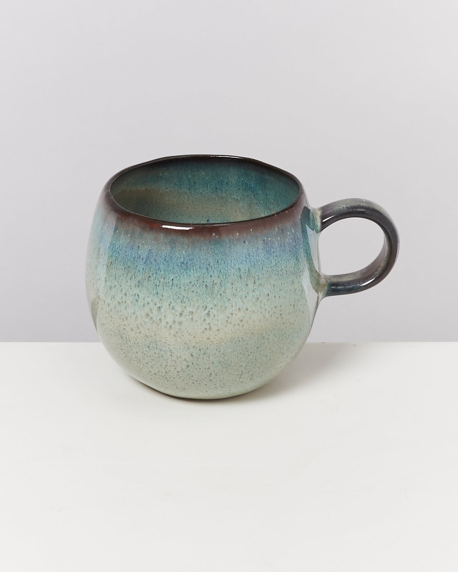 Keramiktasse mit blau-grünem Verlauf und rundem Henkel auf weißem Hintergrund.