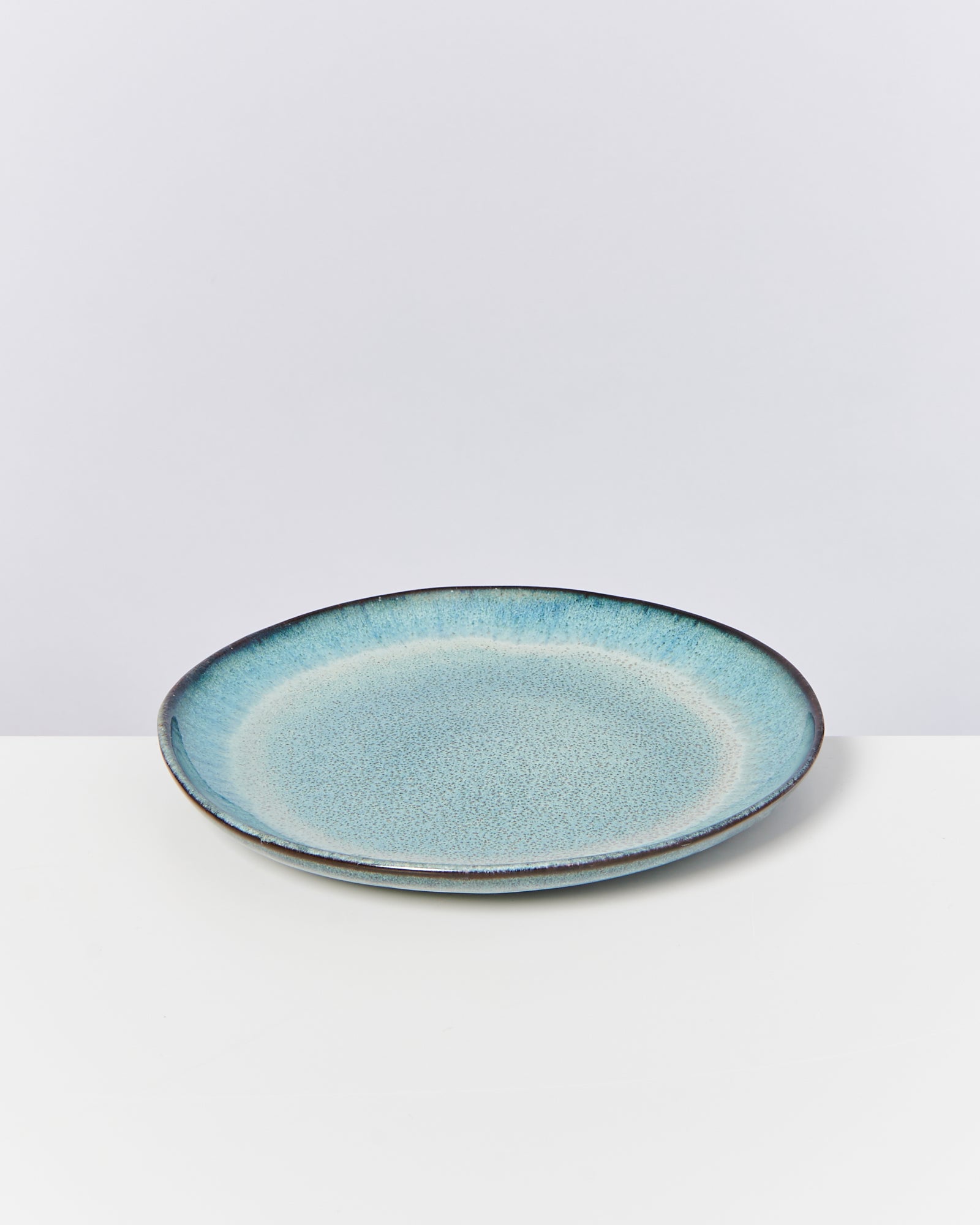 Ein flacher, blauer Keramikteller mit gesprenkeltem Muster auf einem weißen Hintergrund.