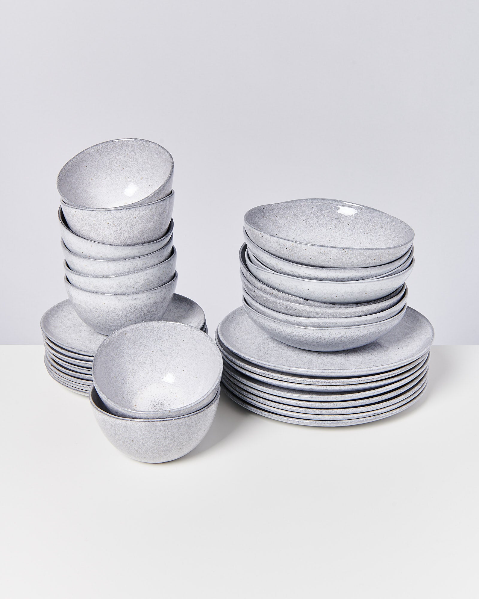 Stapel graue Steingut-Schüsseln und Teller auf einem weißen Tisch.
