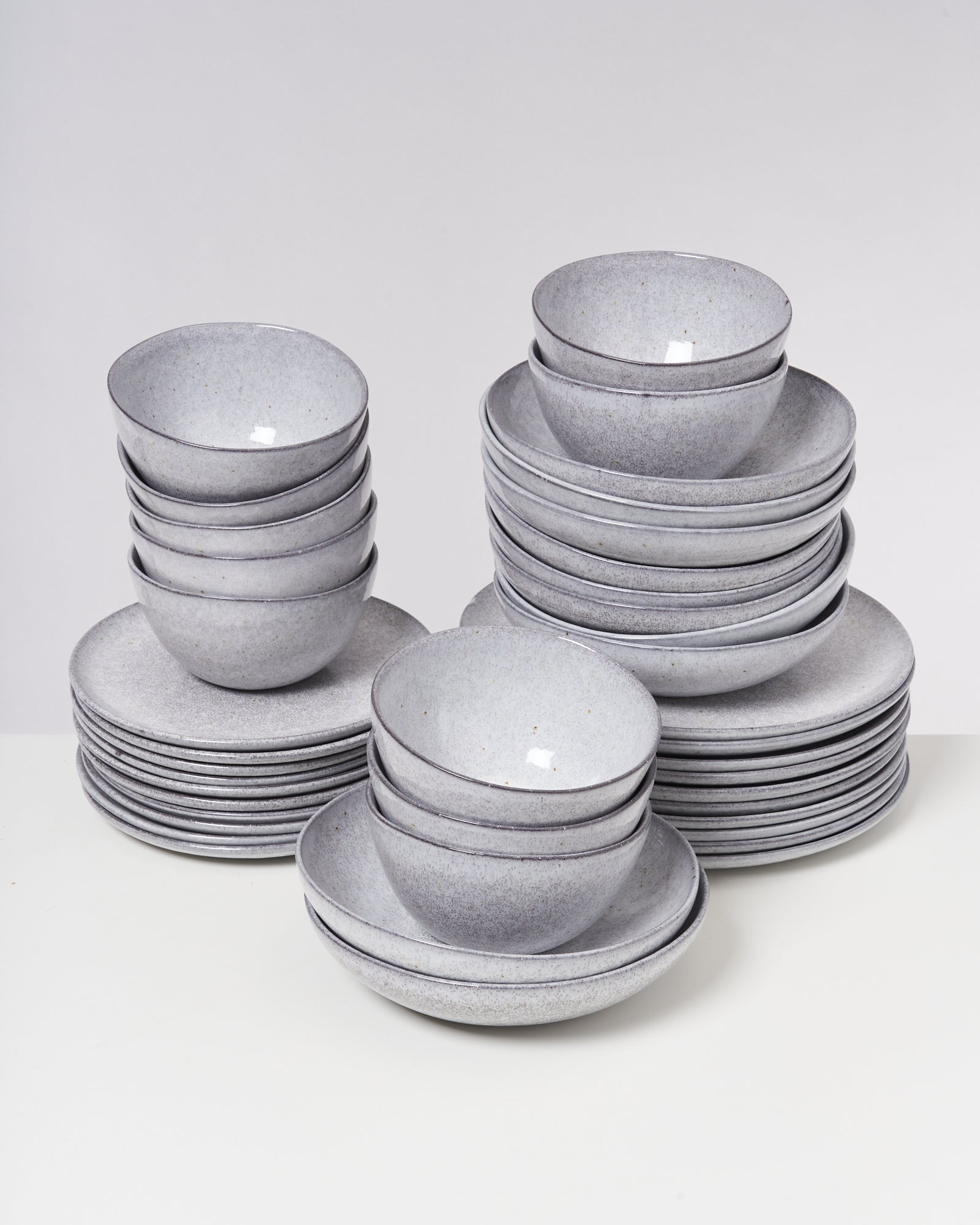 Drei gestapelte Sets grauer Keramikschalen und Teller auf einem weißen Tisch.