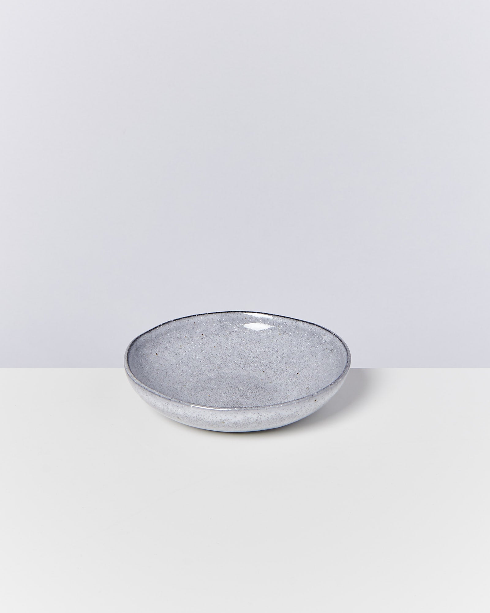 Eine graue Keramikschale steht auf einer weißen Oberfläche vor einem grauen Hintergrund.