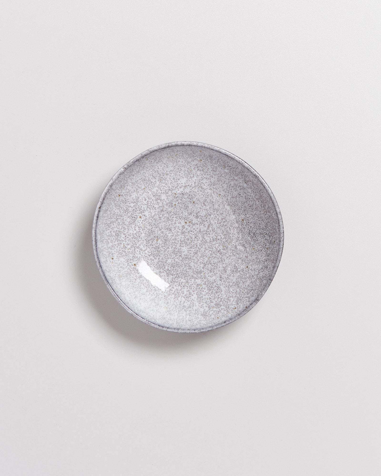Grauer, runder Keramikteller mit gesprenkelter Oberfläche auf weißem Hintergrund.