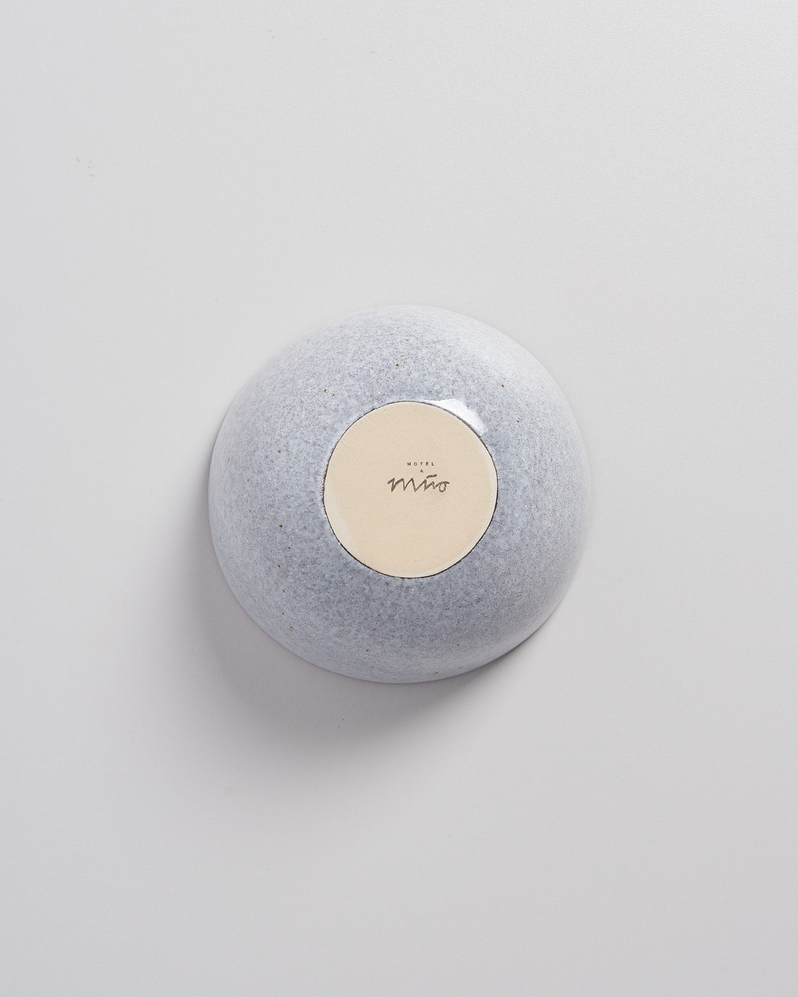 Grauer, runder Stein mit einem beige Etikett auf einer glatten, weißen Oberfläche.