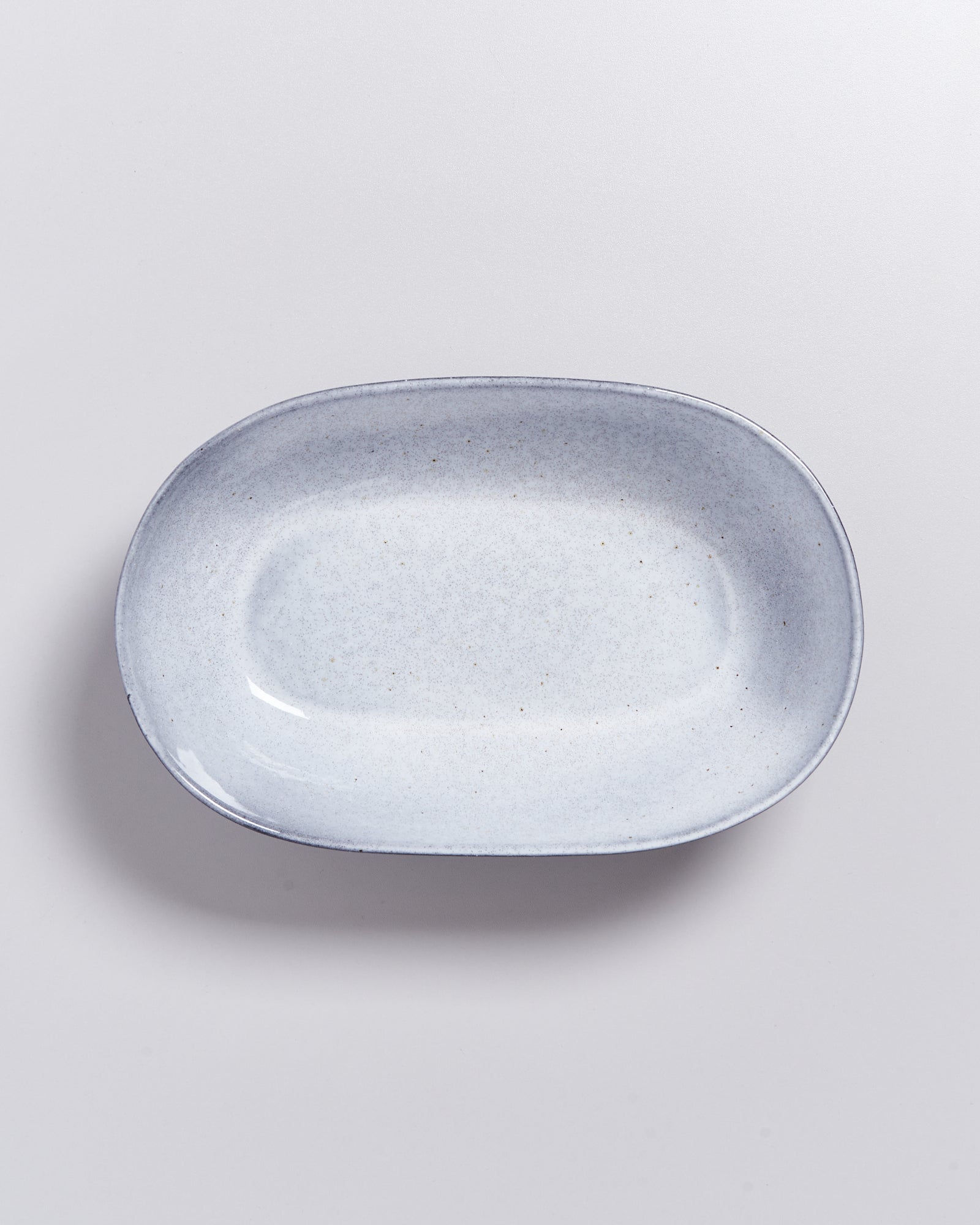 Grauer, ovaler Keramikteller mit einem leichten Sprenkelmuster auf einer hellgrauen Oberfläche.
