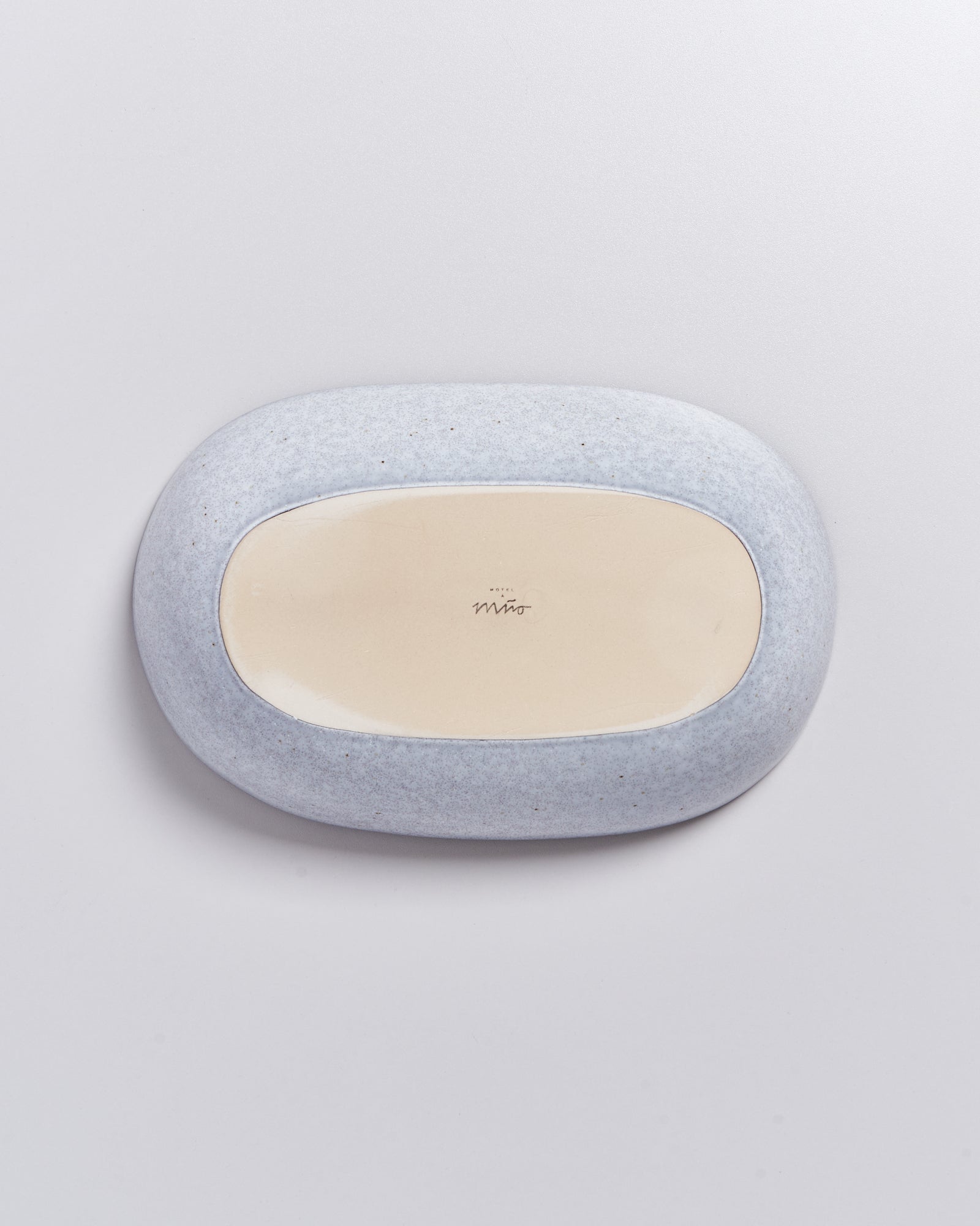 Unterseite eines ovalen Keramikobjekts mit grauer und beige Glasur auf hellem Hintergrund.