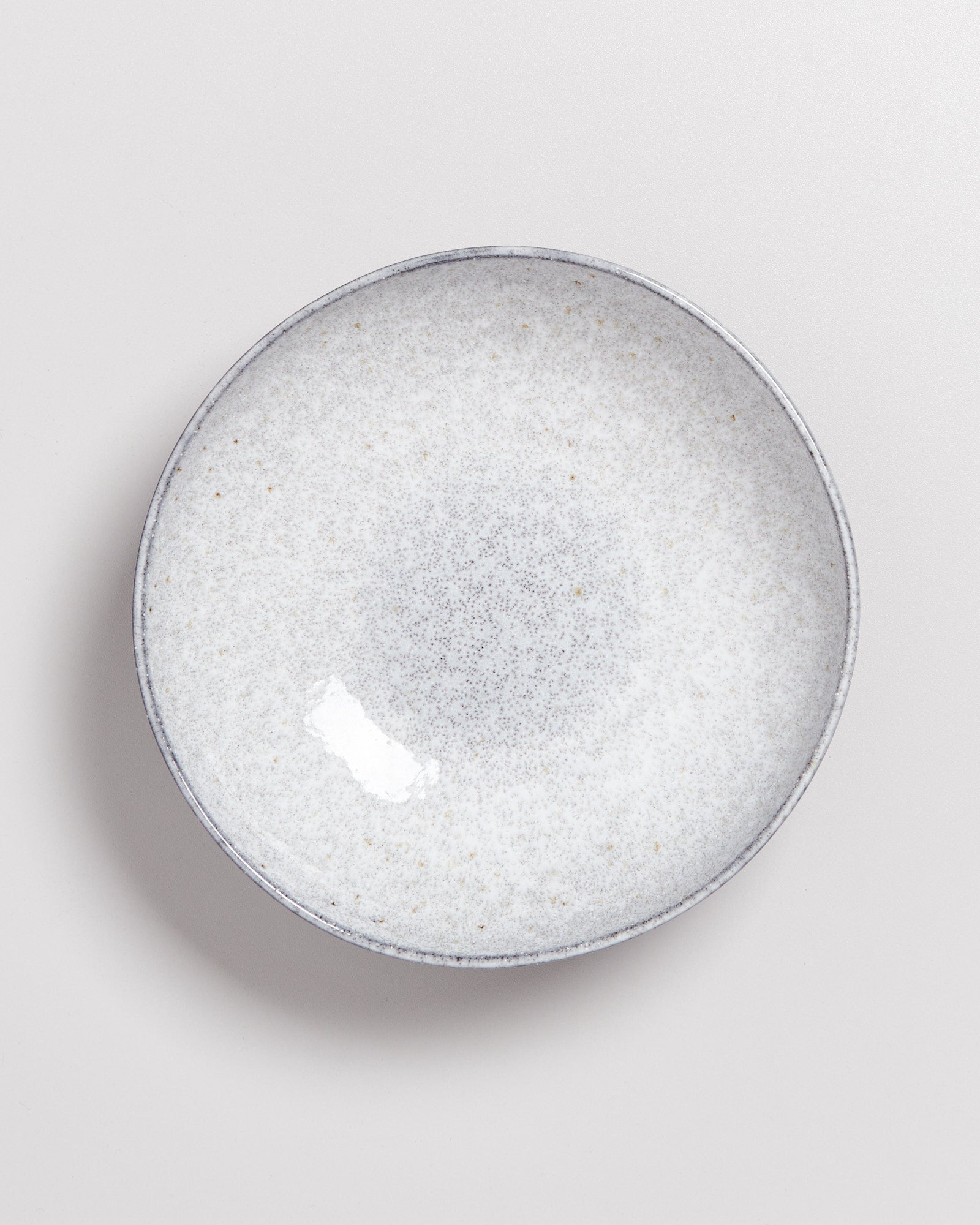 Grauer, gesprenkelter Keramikteller mit minimalistischem Design auf einem weißen Hintergrund.