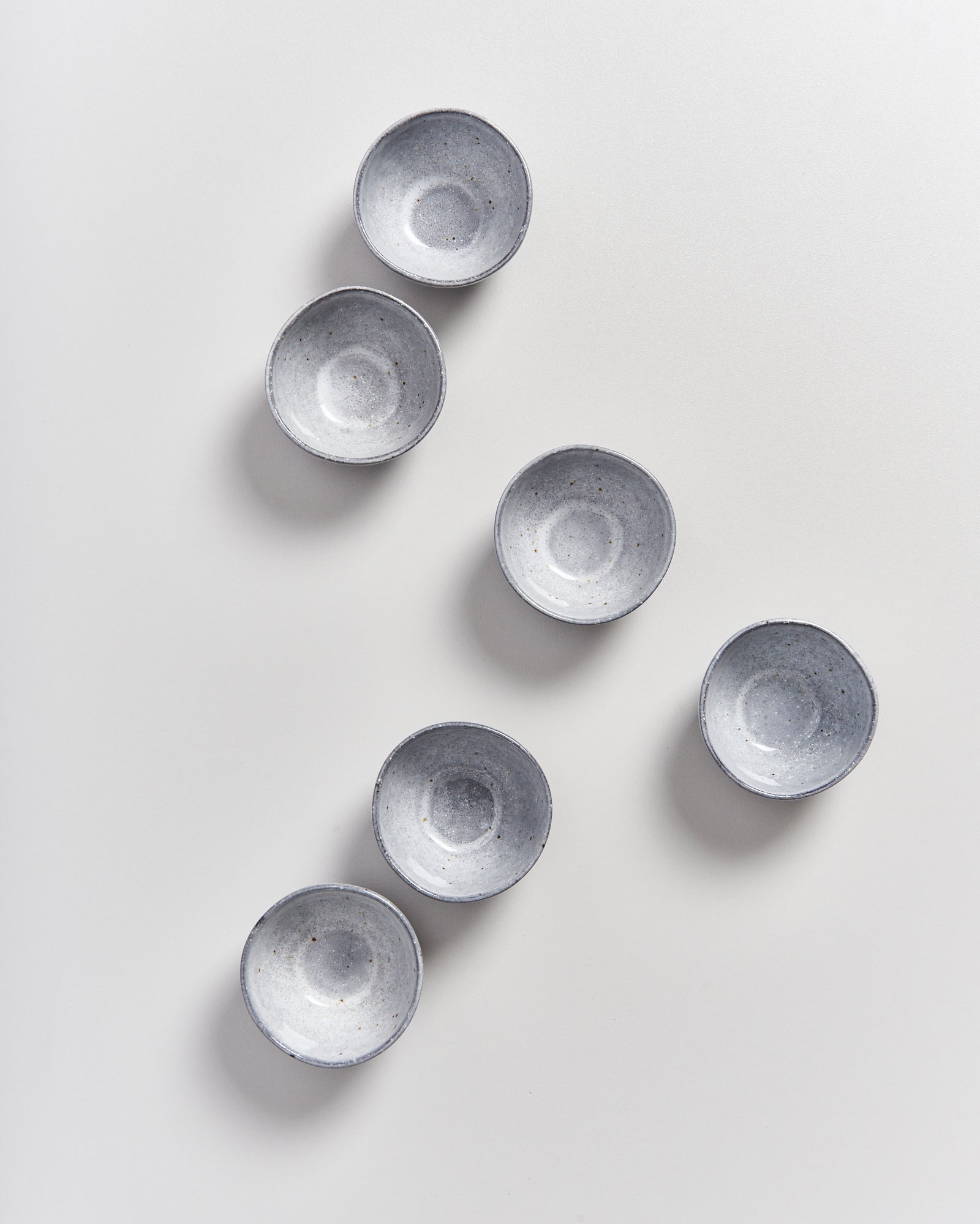 Sechs graue, runde Schalen sind auf einem weißen Hintergrund in einem Zickzack-Muster angeordnet.