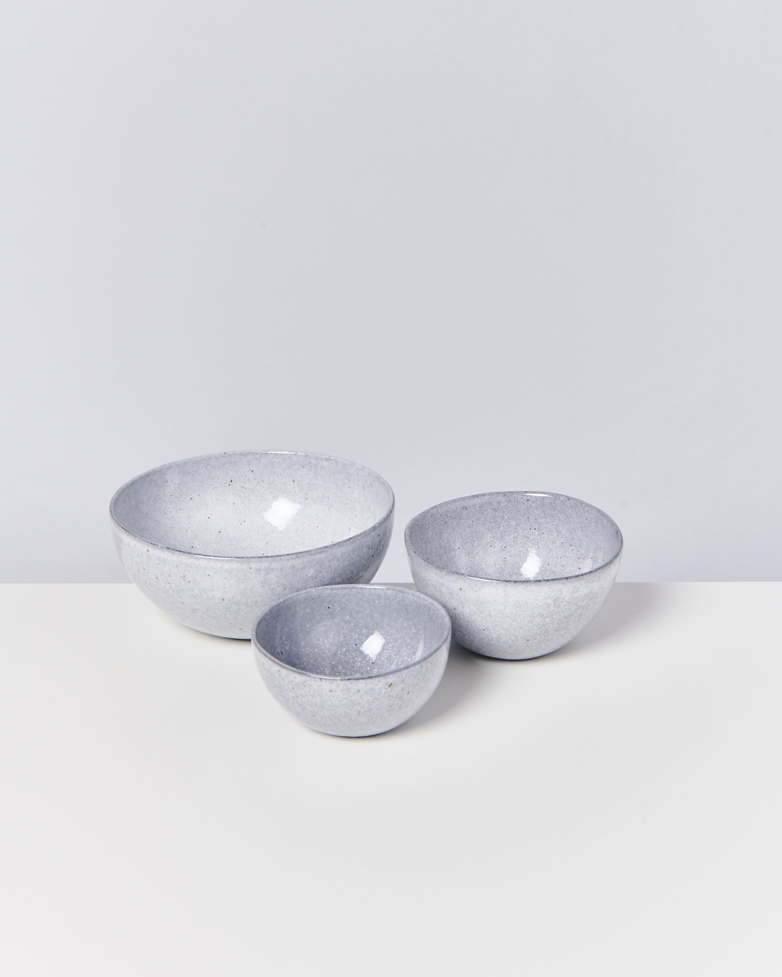 Drei graue Keramikschalen unterschiedlicher Größe stehen auf einem weißen Untergrund vor einem hellgrauen Hintergrund.