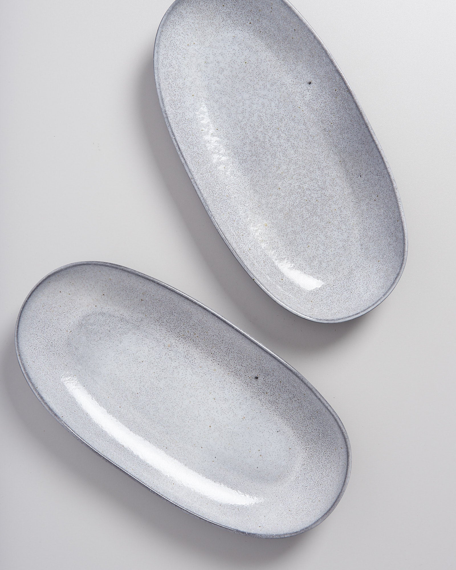 Zwei ovale, hellgraue Keramikteller mit gesprenkelter Oberfläche auf einer weißen Fläche.