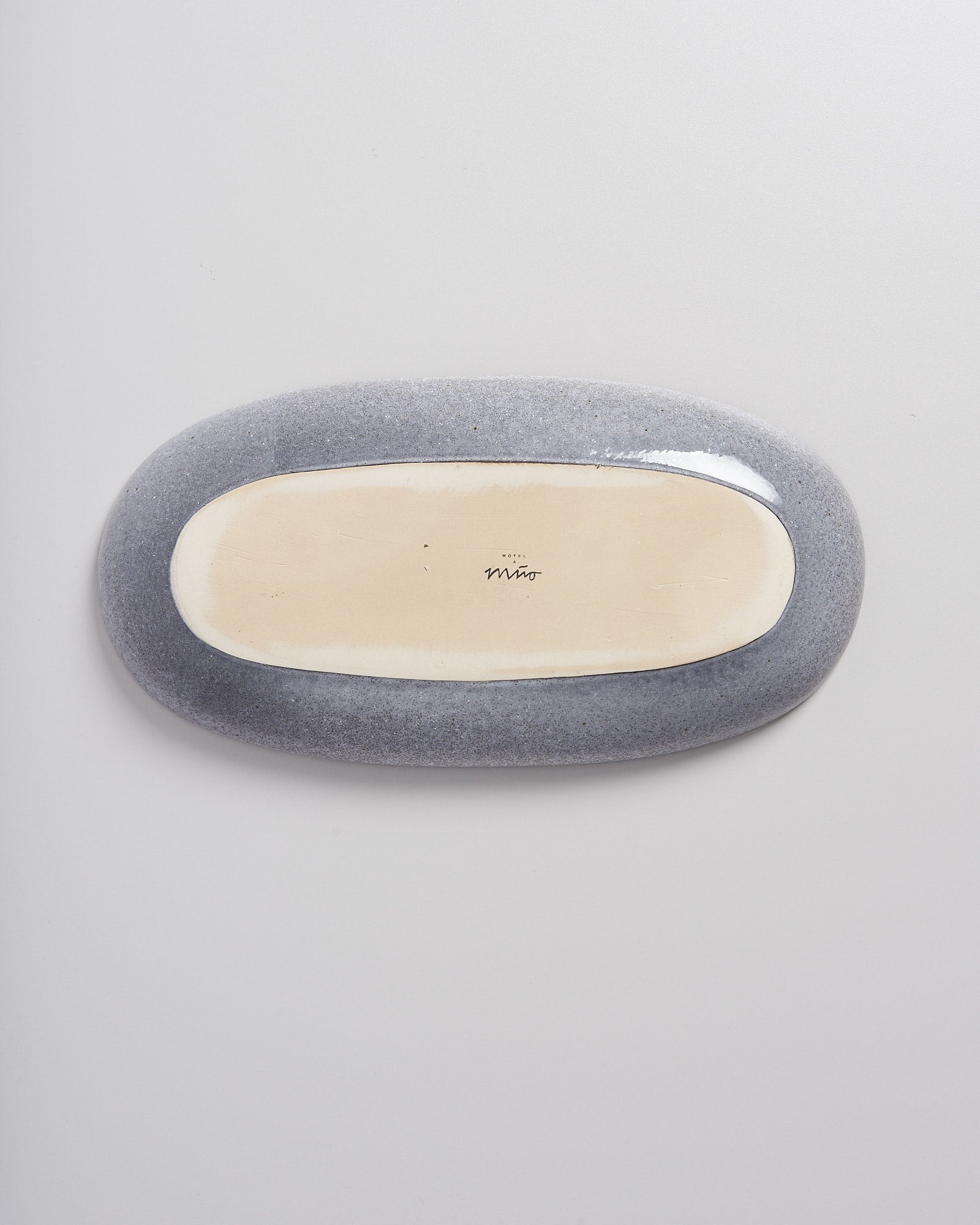 Ovaler Keramikgegenstand mit grauer Außenseite und beigem Boden auf weißem Hintergrund.