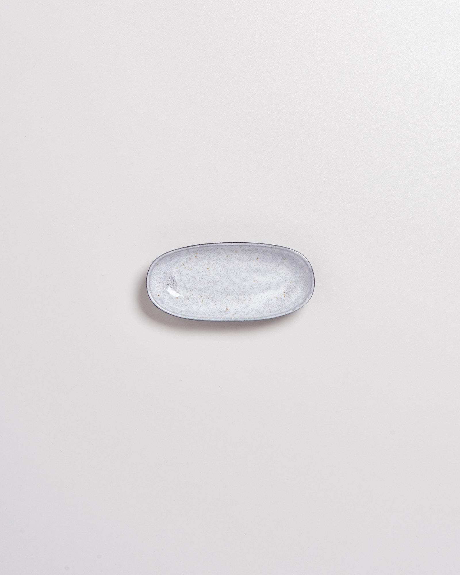Kleiner, ovaler, grauer Keramikteller auf einem hellgrauen Hintergrund.