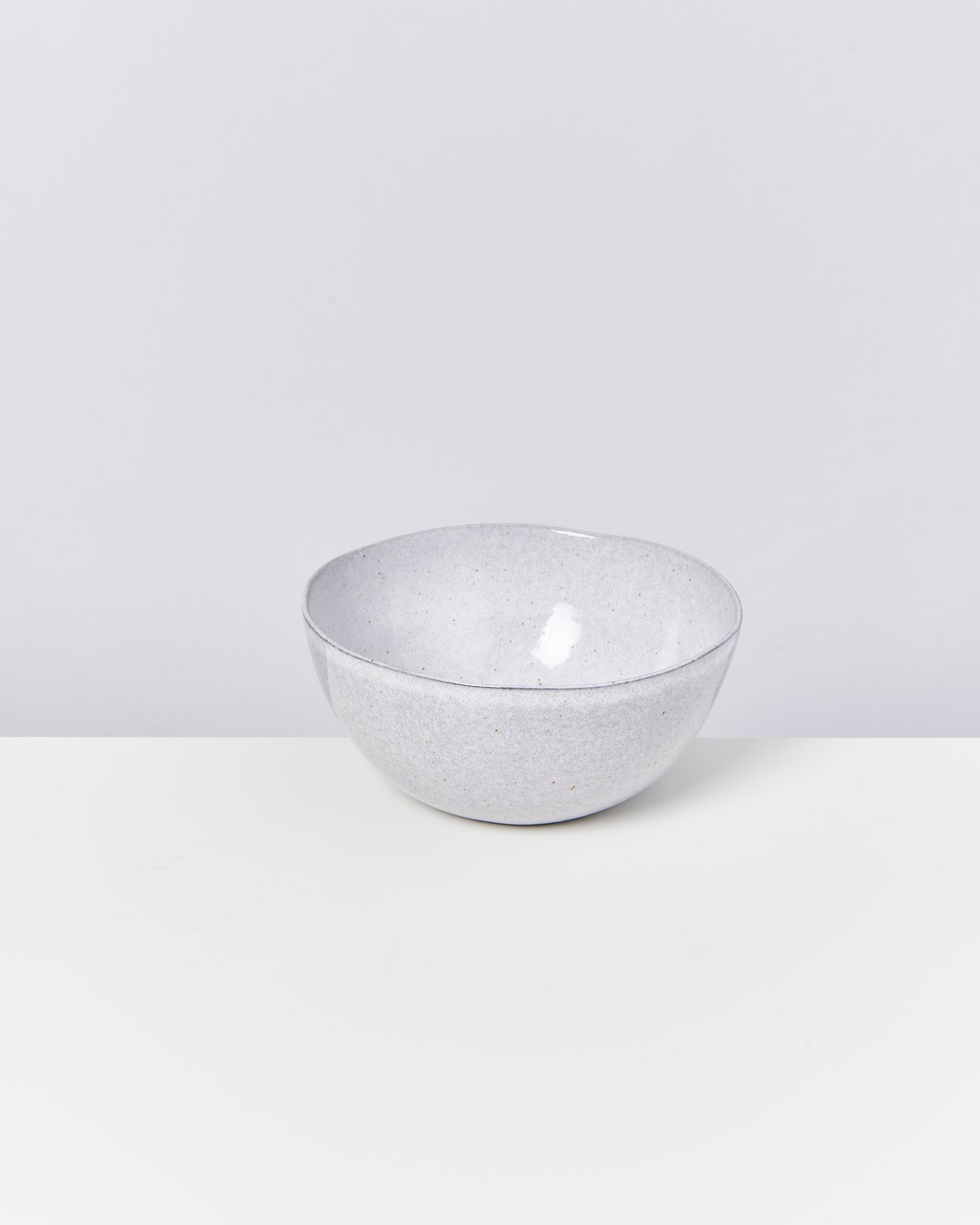 Graue Keramikschale steht auf einem weißen Tisch vor einem hellgrauen Hintergrund.