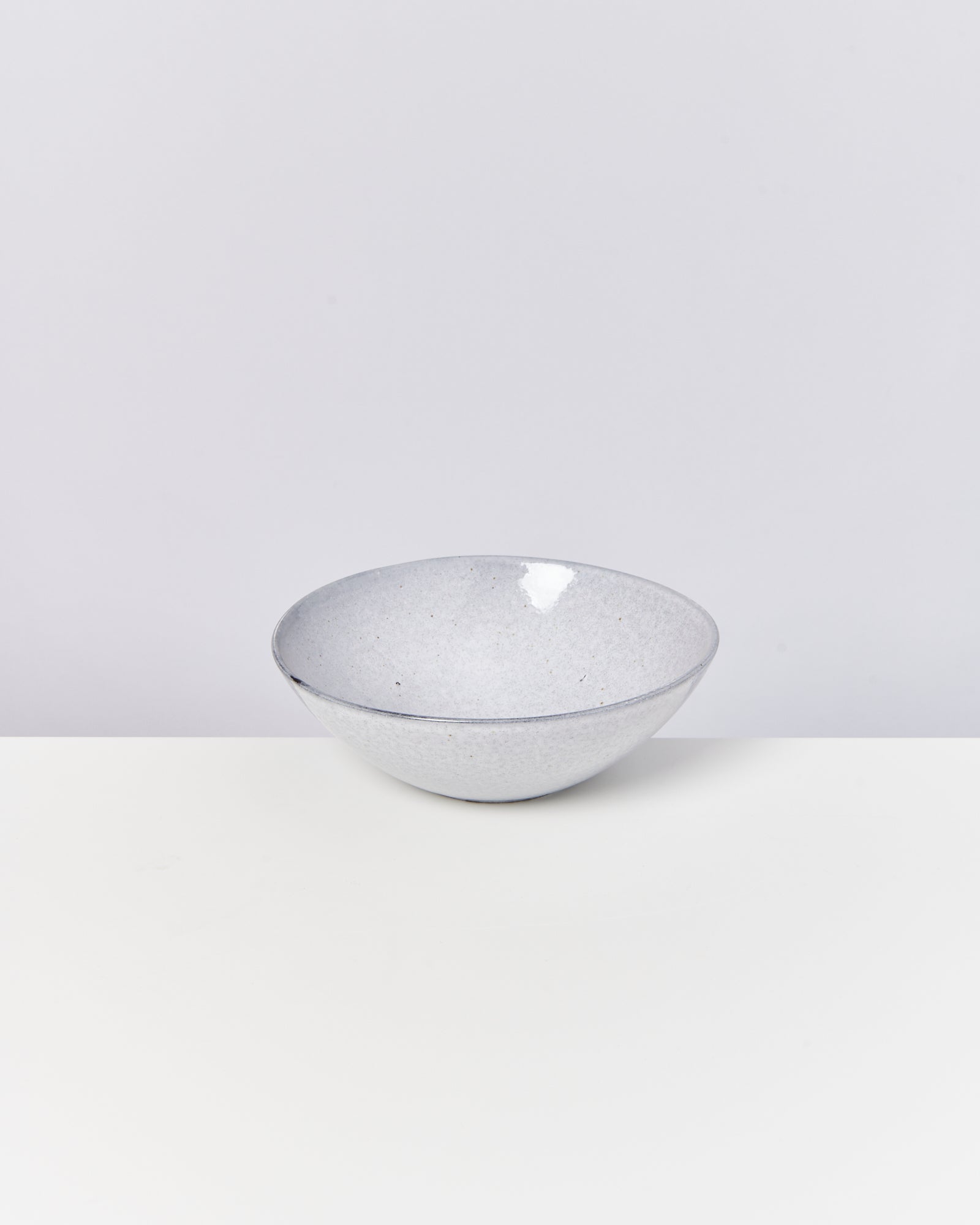 Grau melierte Schüssel aus Keramik auf einem weißen Tisch, vor einem hellgrauen Hintergrund platziert.