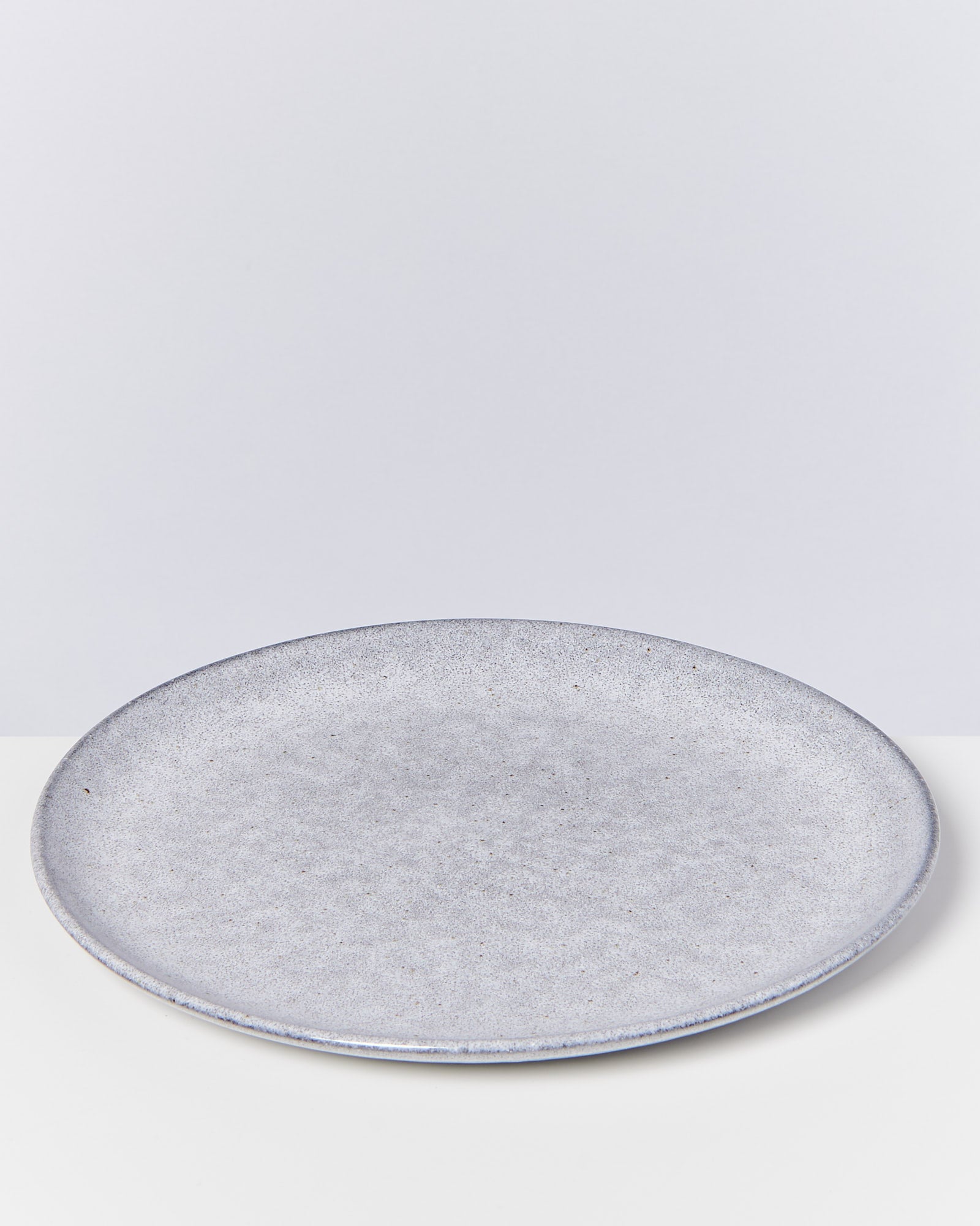 Grauer, flacher Keramikteller auf weißem Hintergrund.