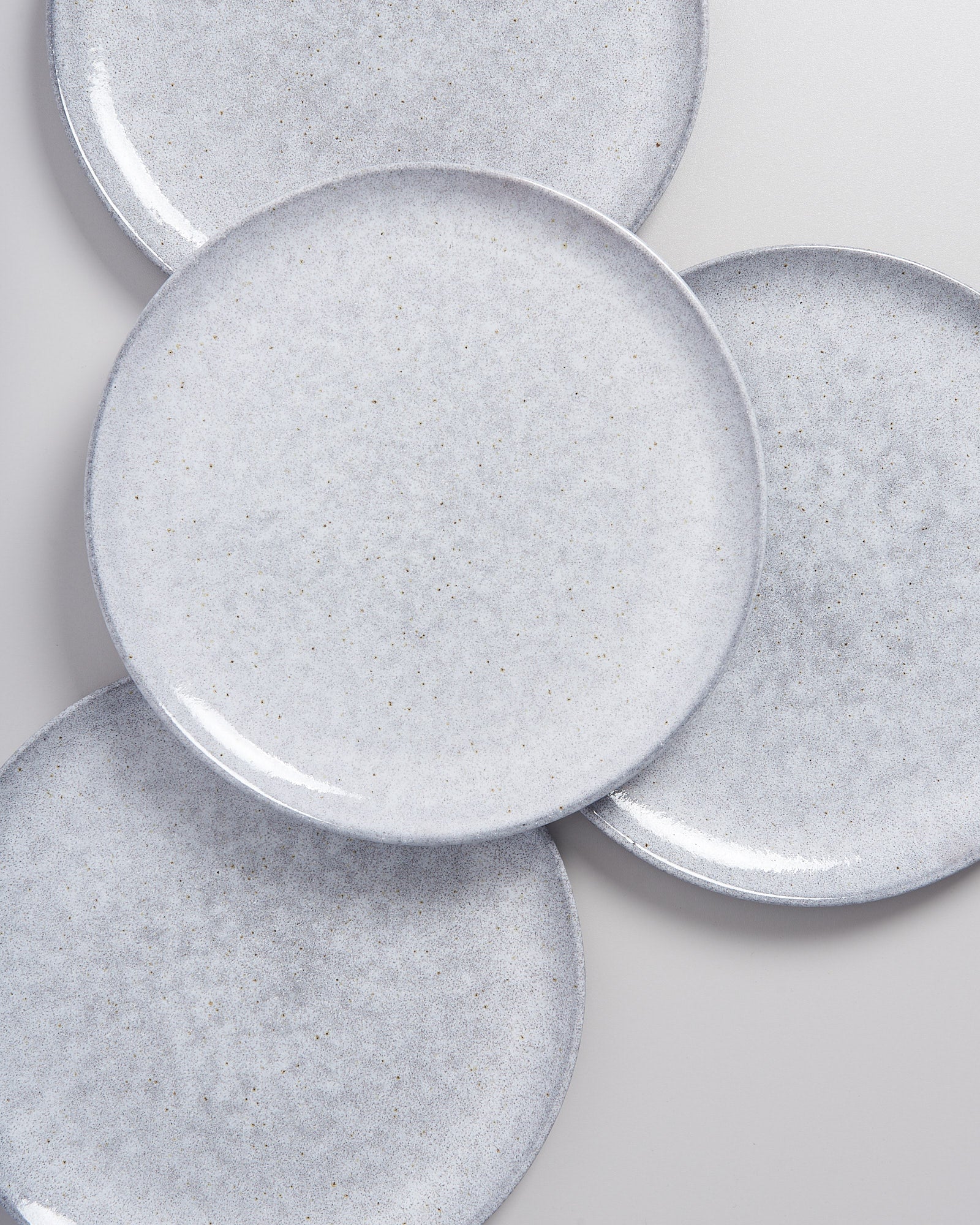 Vier graue Keramikteller mit feiner Sprenkelung liegen überlappend auf einer weißen Oberfläche.