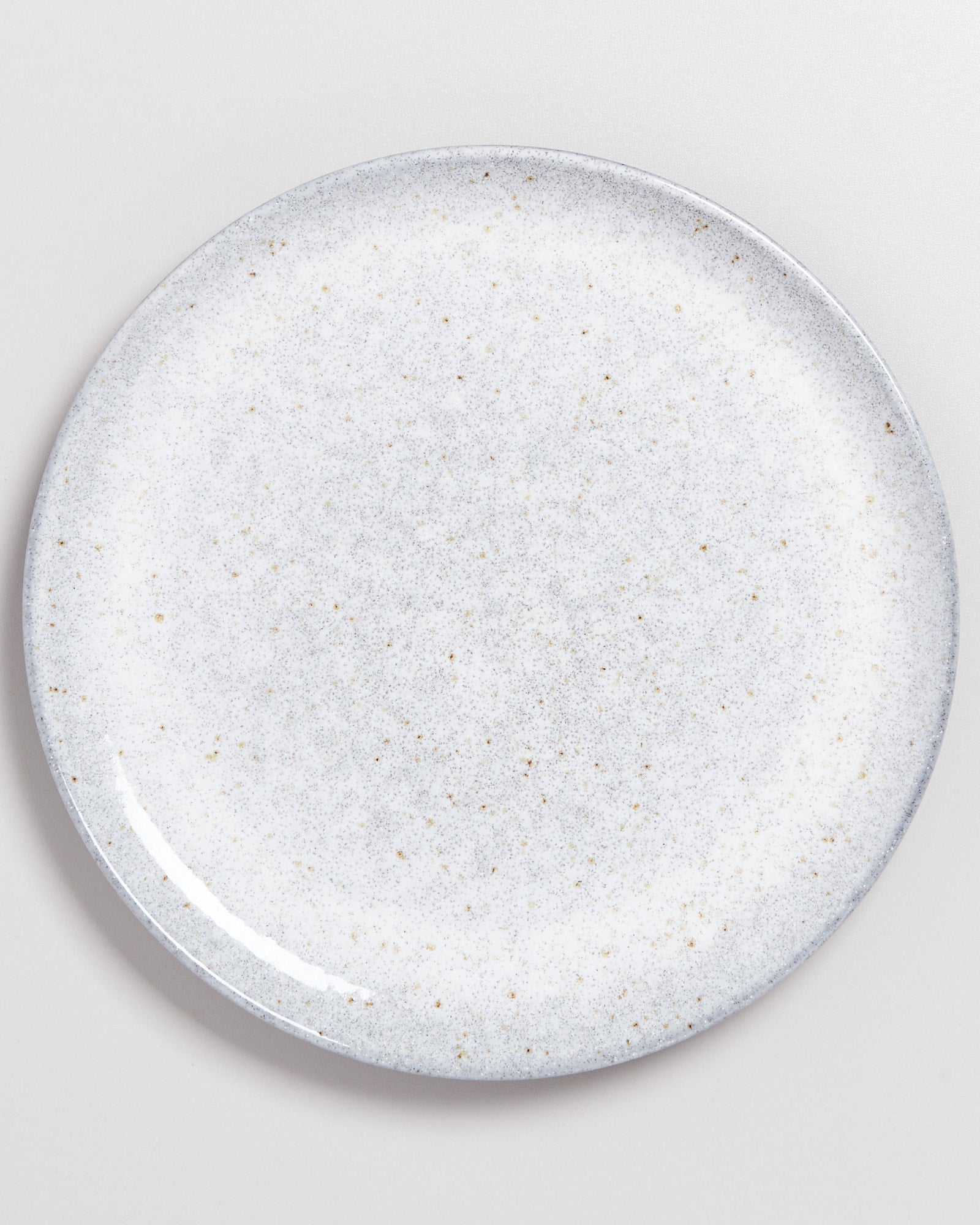 Eine runde, gesprenkelte graue und weiße Keramikplatte auf einer hellgrauen Oberfläche.