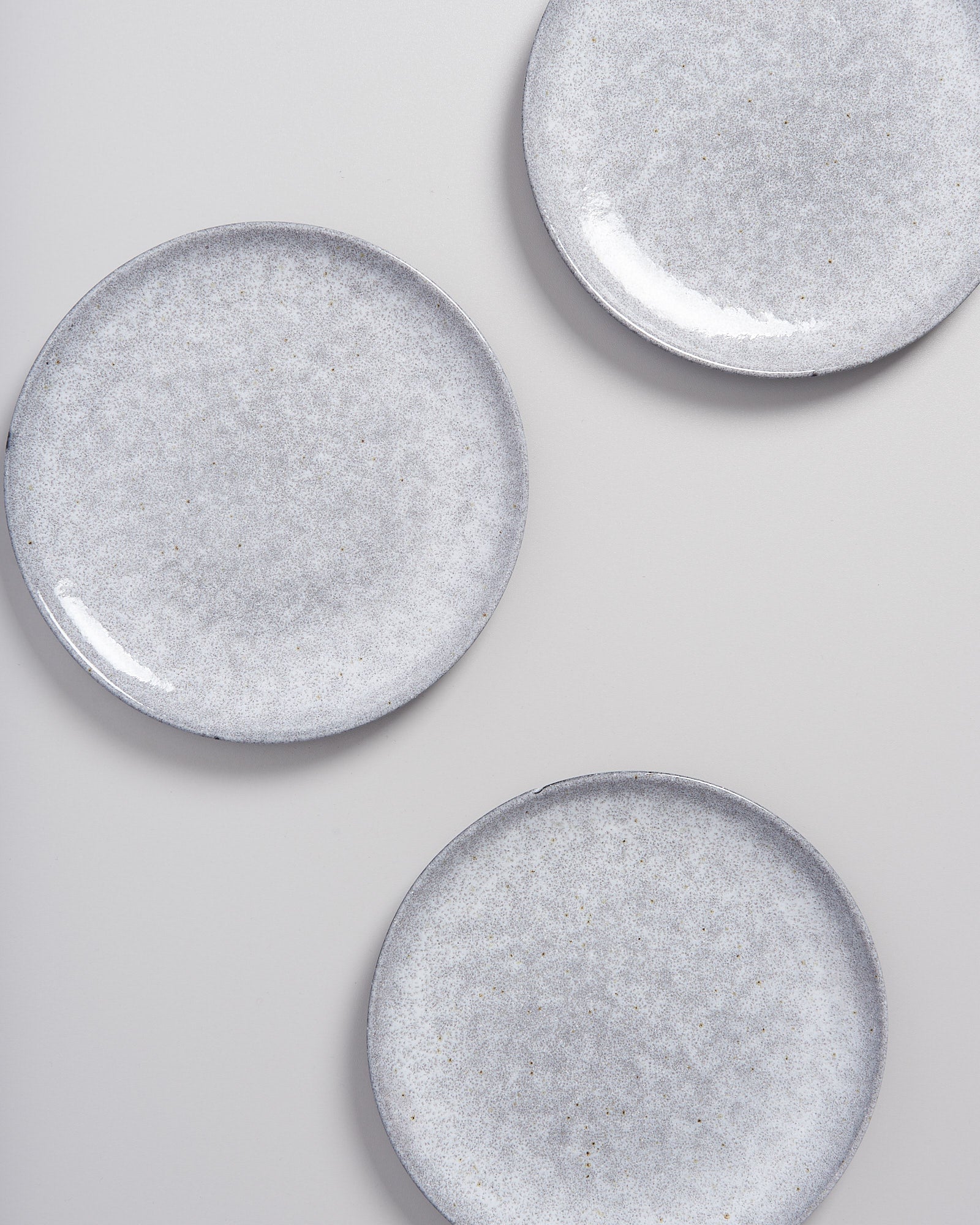 Drei graue, gesprenkelte Teller liegen auf einer hellen, glatten Oberfläche.