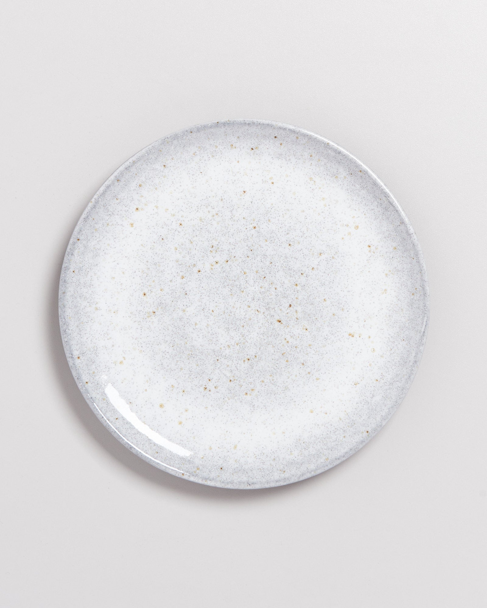 Grauer Keramikteller mit gesprenkeltem Muster auf hellem Hintergrund.