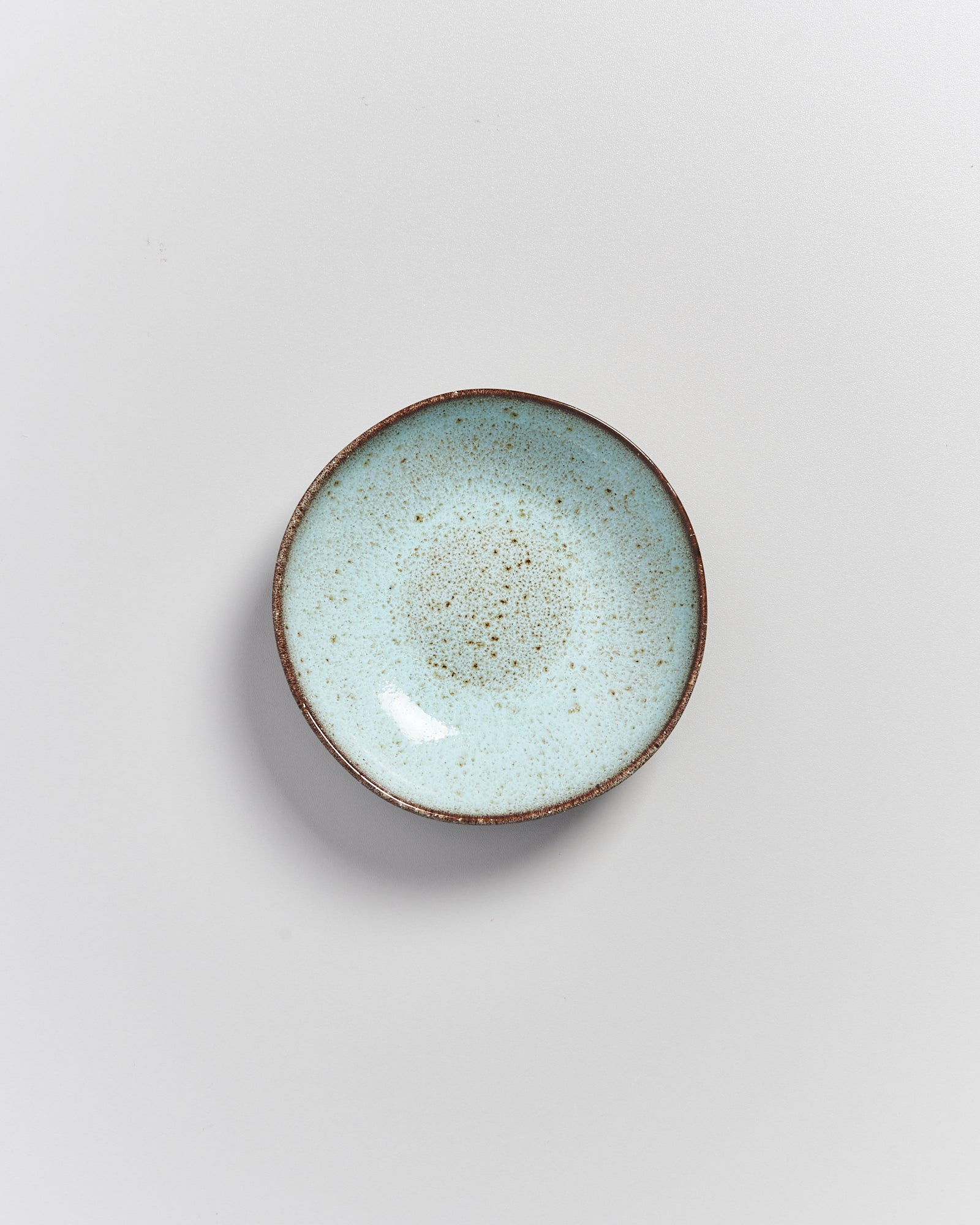 Kleine, runde, hellblaue Keramikschale mit braunem Rand auf weißem Hintergrund.