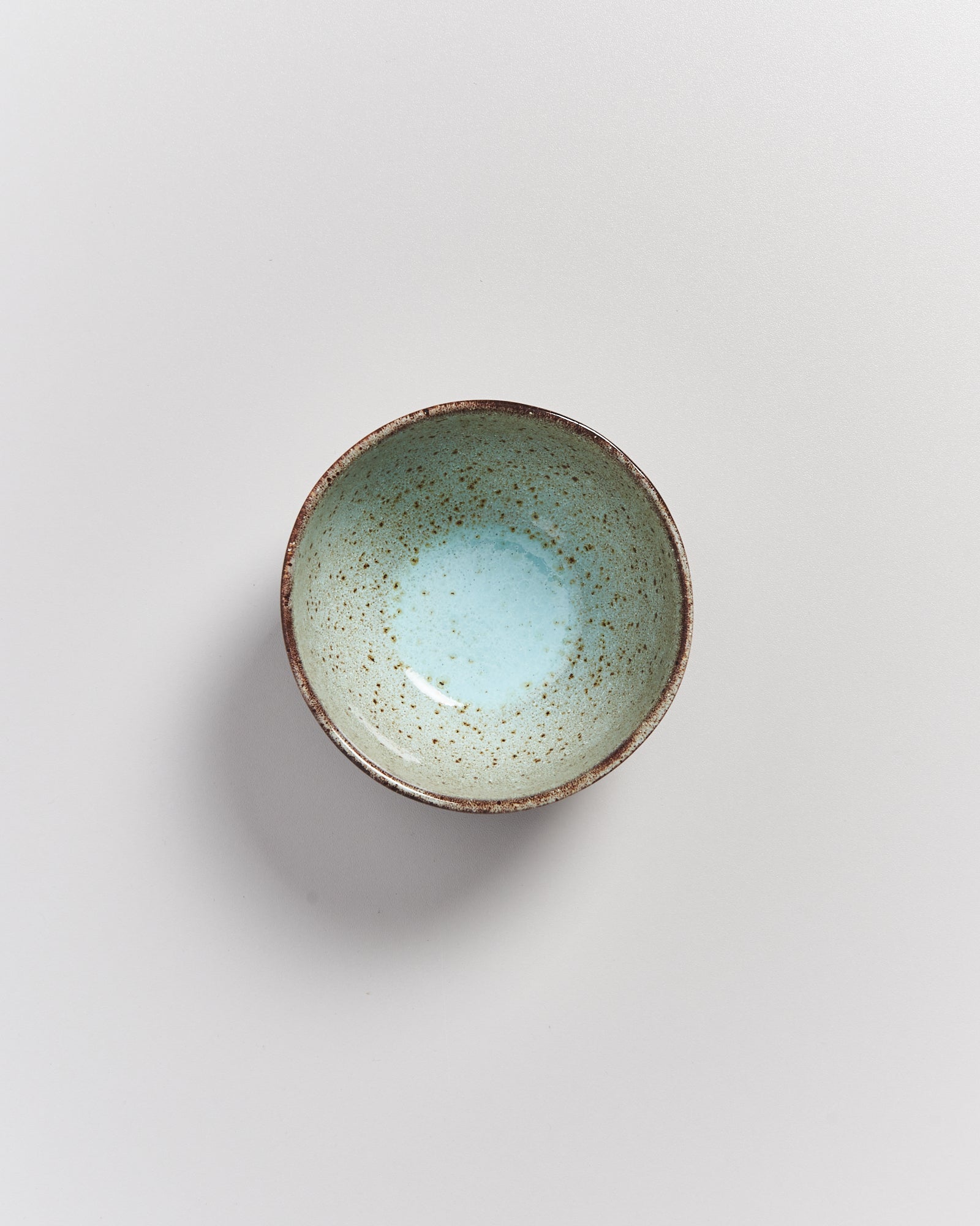 Keramikschale mit gesprenkeltem, hellblauem Innenraum auf grauem Hintergrund.