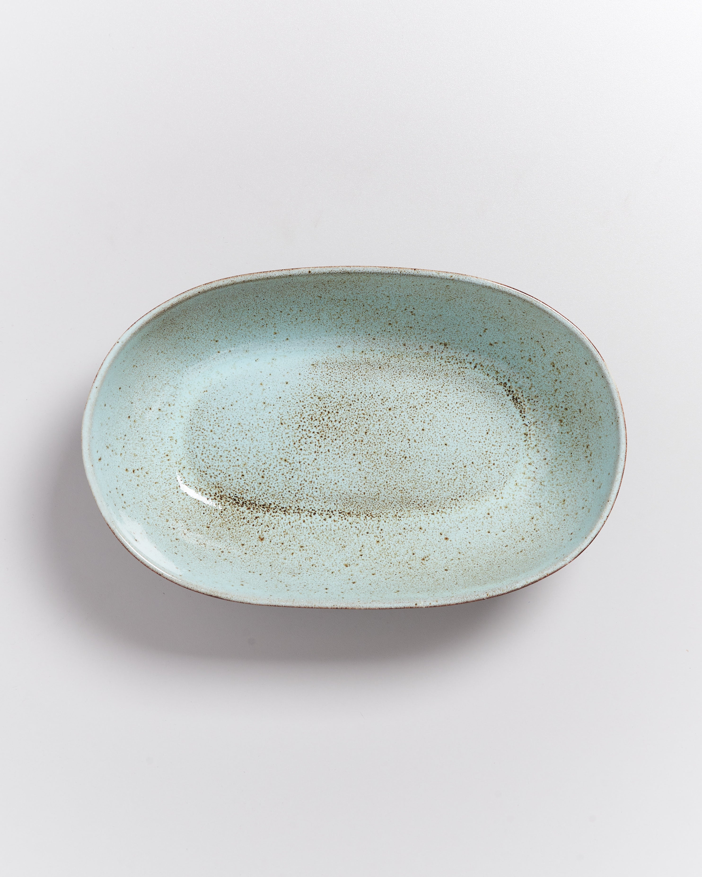 Ovale, hellblaue Keramikschale mit gesprenkelter Oberfläche auf weißem Hintergrund.