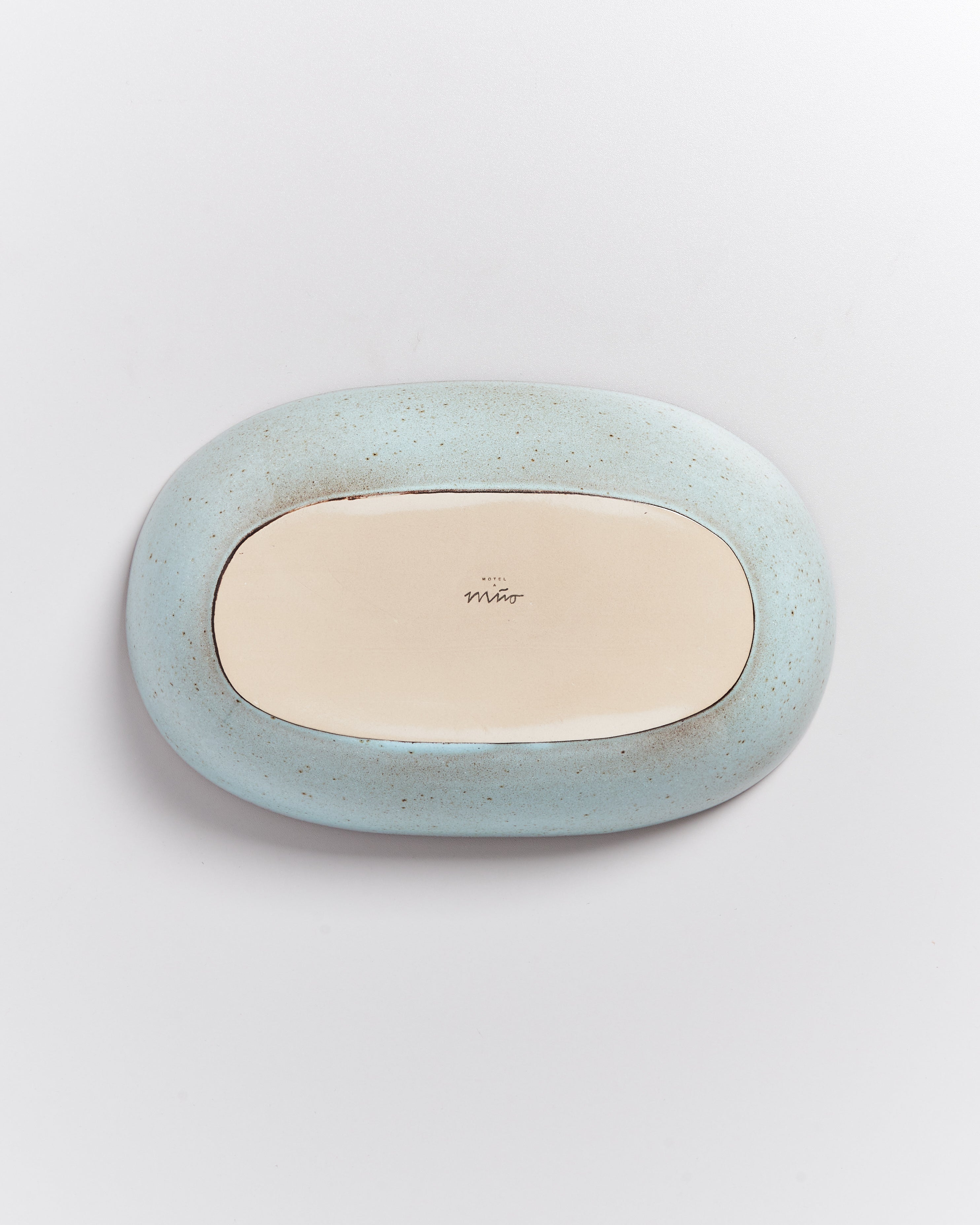 Ovaler, blauer Porzellanteller mit beiger Innenseite und einer kleinen Beschriftung in der Mitte.