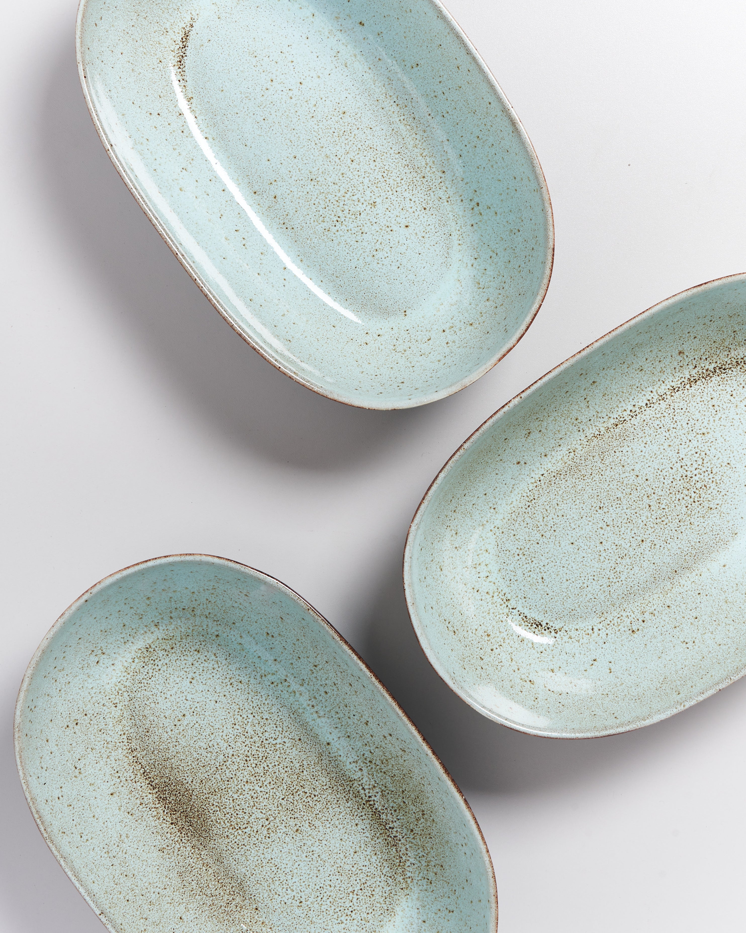 Drei olivgrüne, ovale Keramikteller mit gesprenkeltem Muster auf weißem Hintergrund.