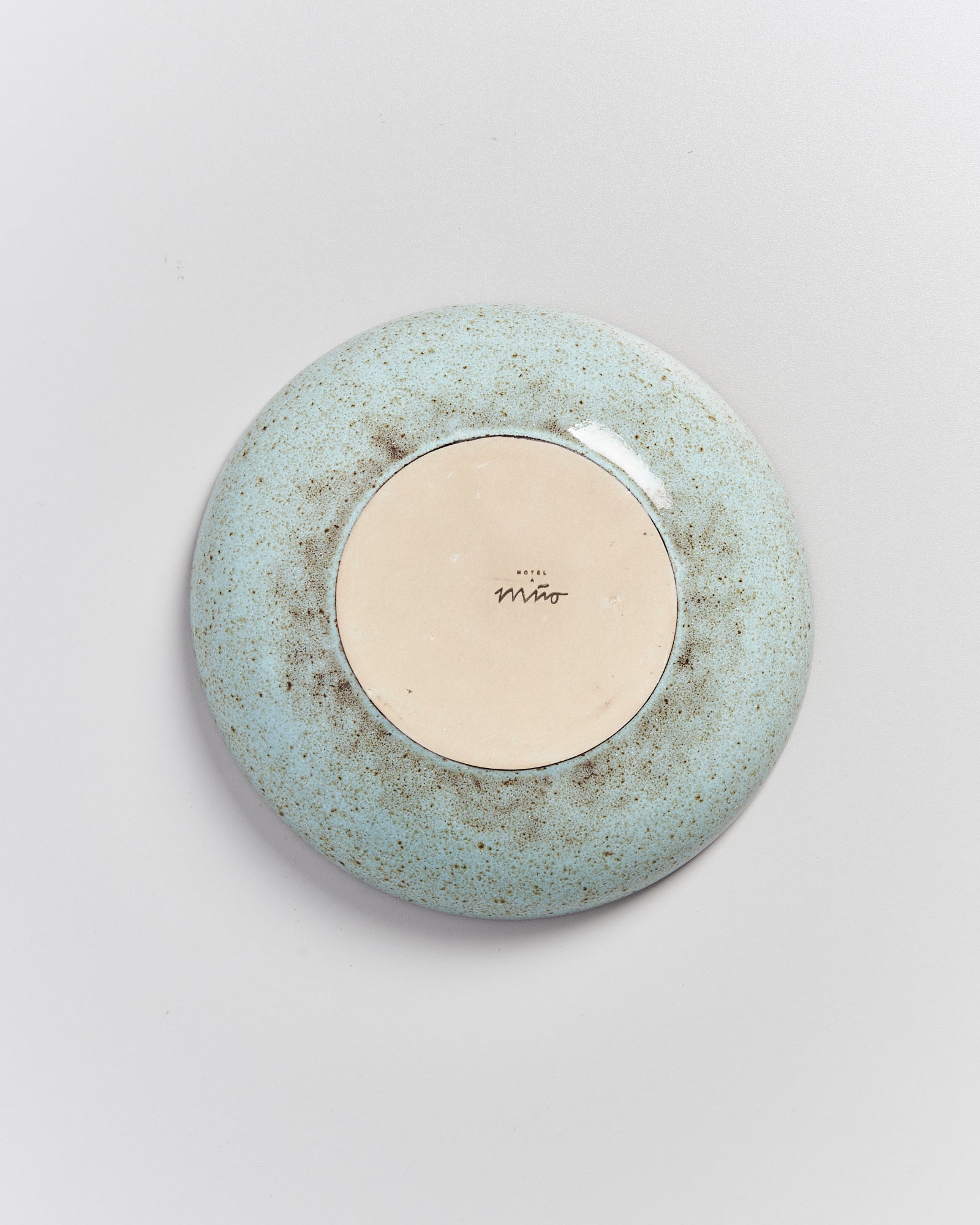 Die Rückseite eines runden Keramiktellers mit blau-grüner Glasur und der Aufschrift "Hotel Miro" in der Mitte.