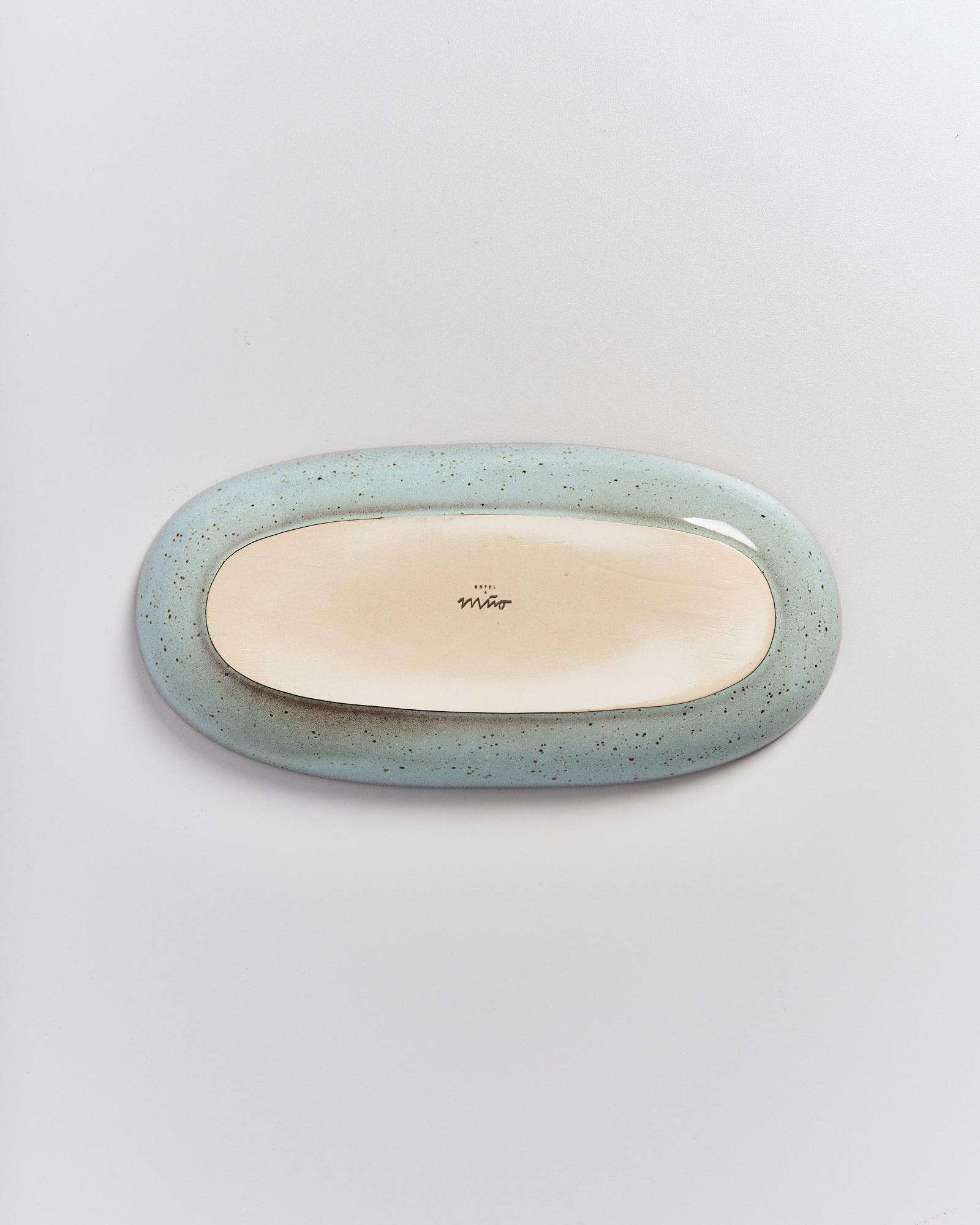 Ovale, blau gesprenkelte Keramikschale auf weißem Hintergrund, auf der Unterseite ein kleiner, handgeschriebener Schriftzug.