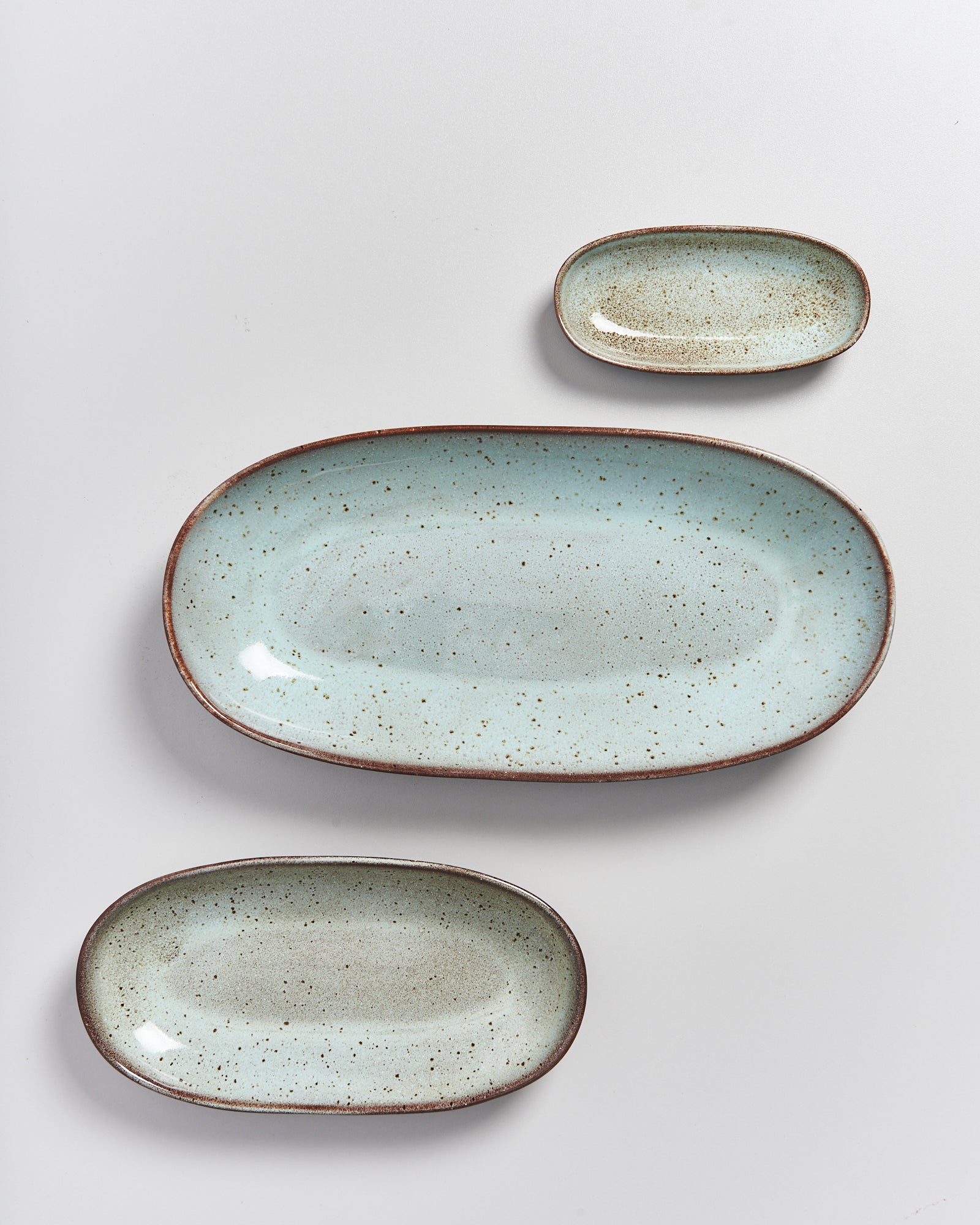 Drei ovale, türkisfarbene Teller in verschiedenen Größen auf weißem Hintergrund.