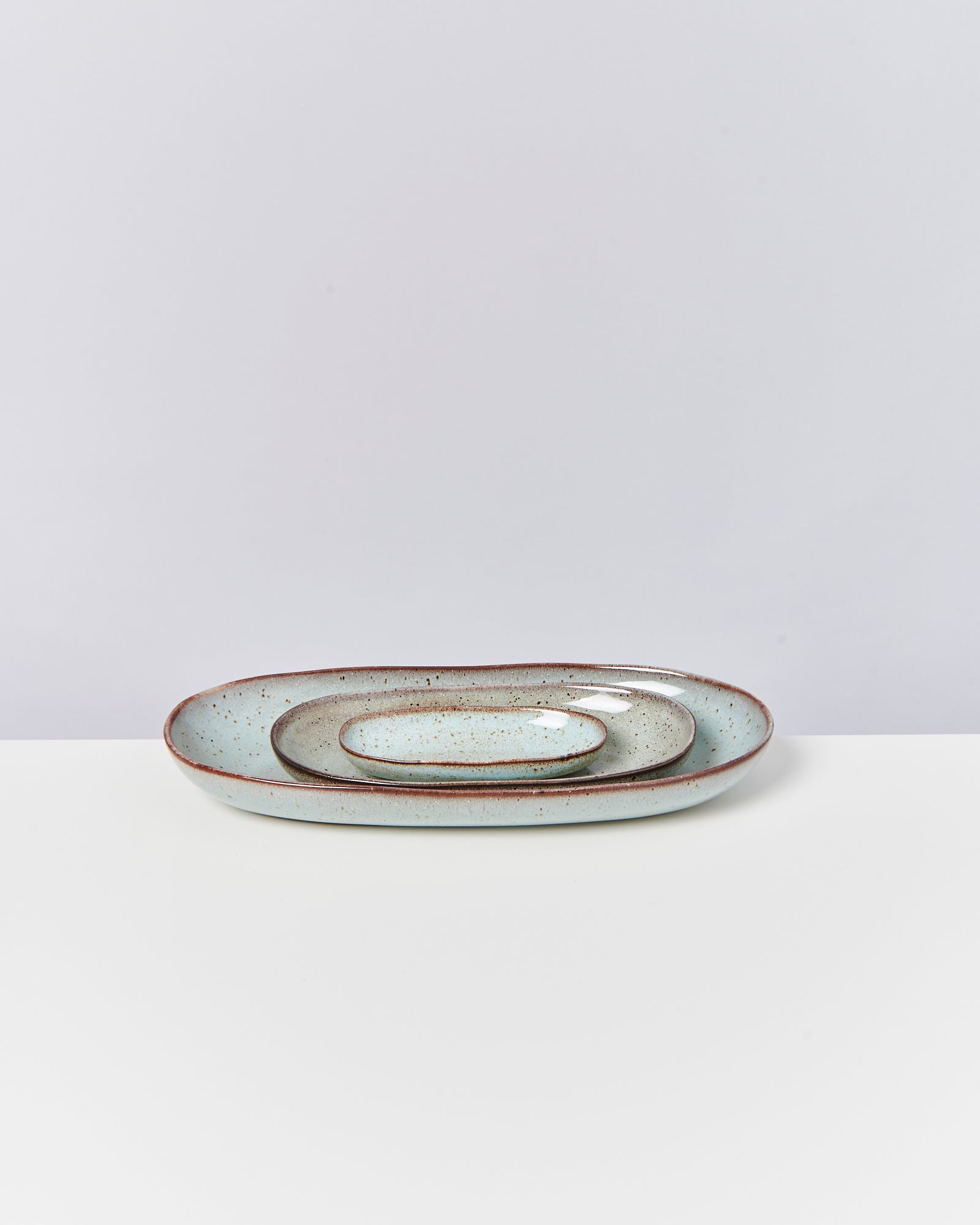 Zwei ovale, grünliche Teller mit rustikaler Glasur liegen auf einem weißen Untergrund.