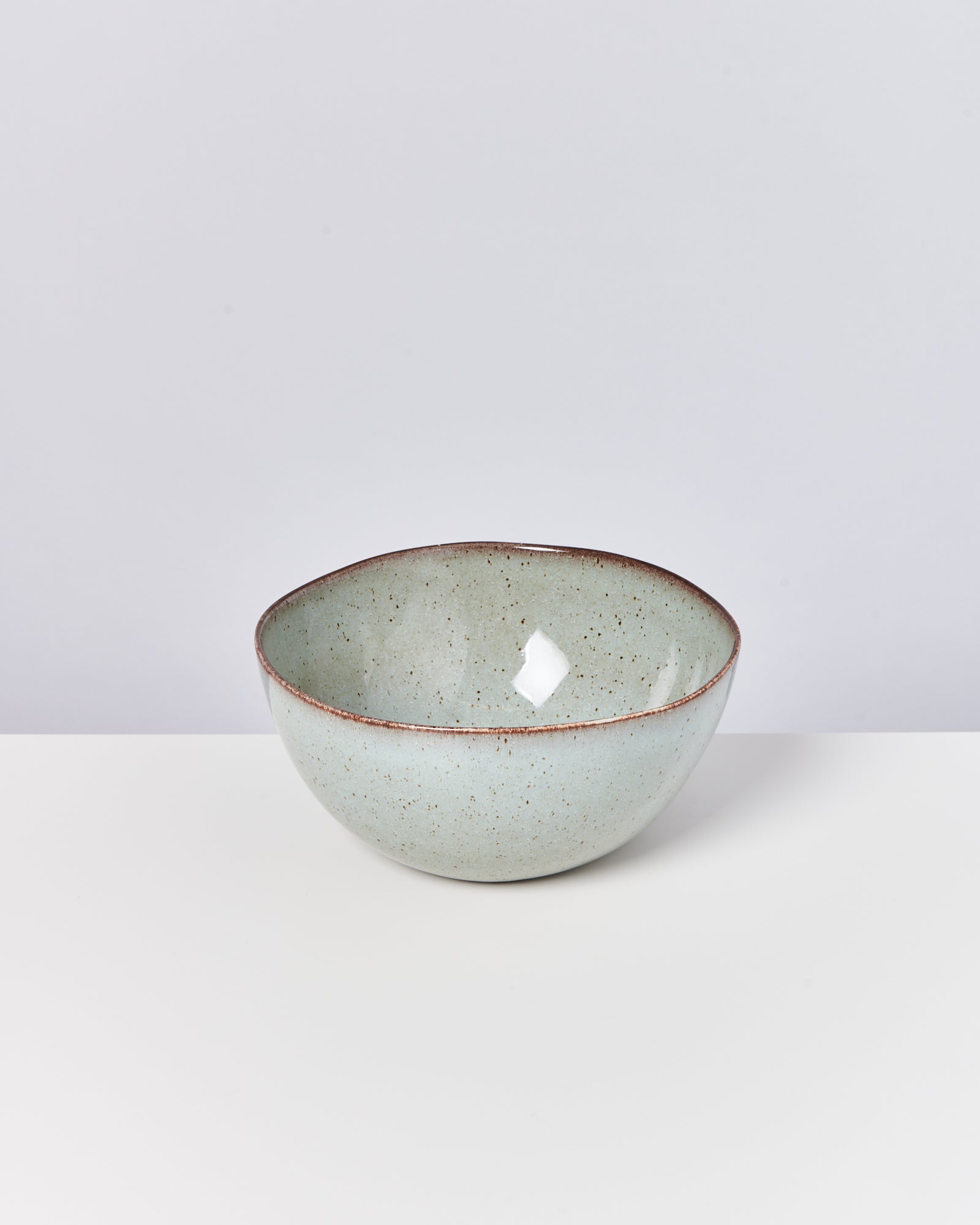 Keramikschüssel mit grüner Glasur und braunem Rand auf weißem Hintergrund.