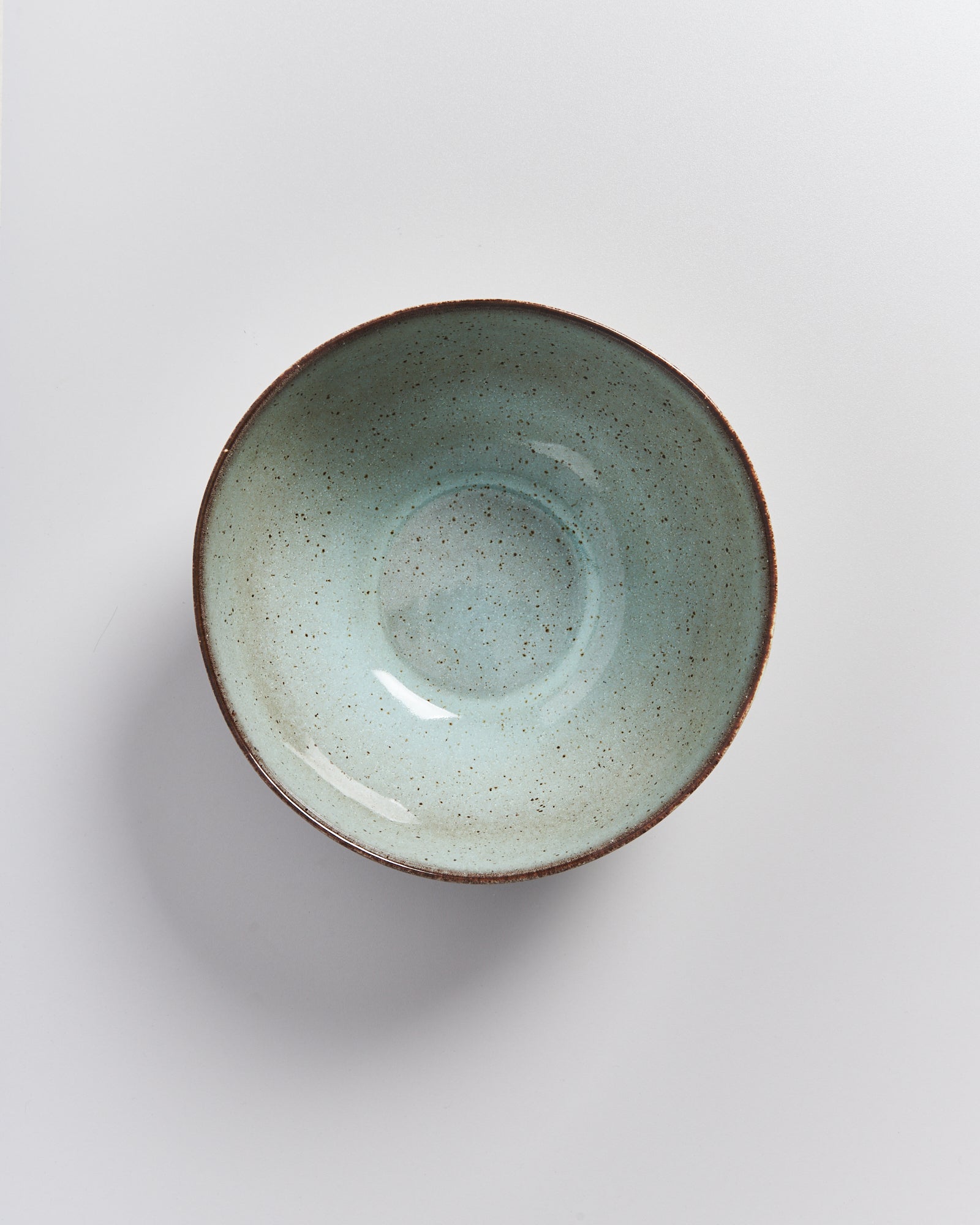 Eine Keramikschüssel mit hellblauer Glasur und braunem Rand auf einem weißen Hintergrund.