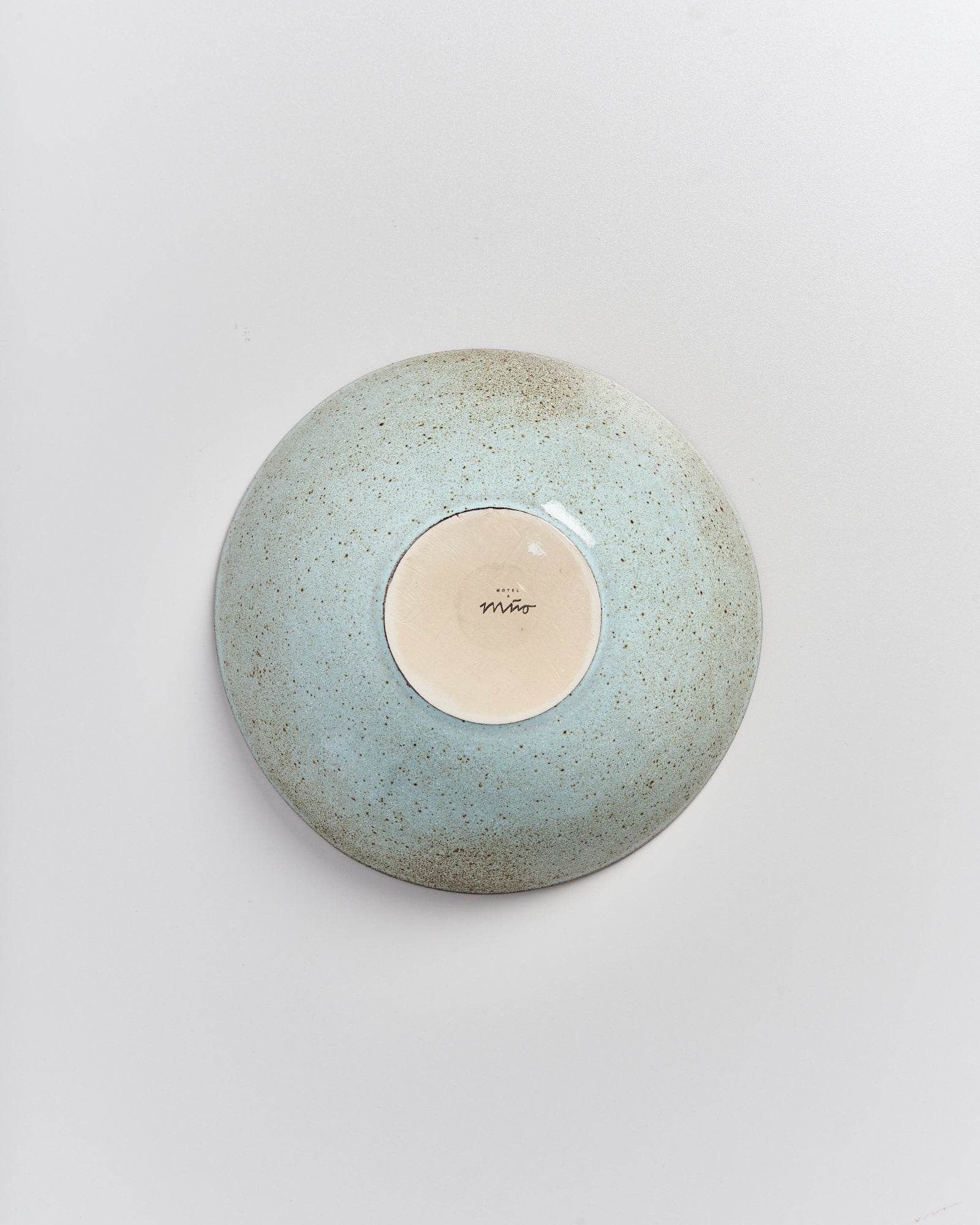 Eine umgedrehte, hellblaue Keramikschale mit gesprenkelter Oberfläche und einer Signatur auf der Unterseite auf weißem Hintergrund.