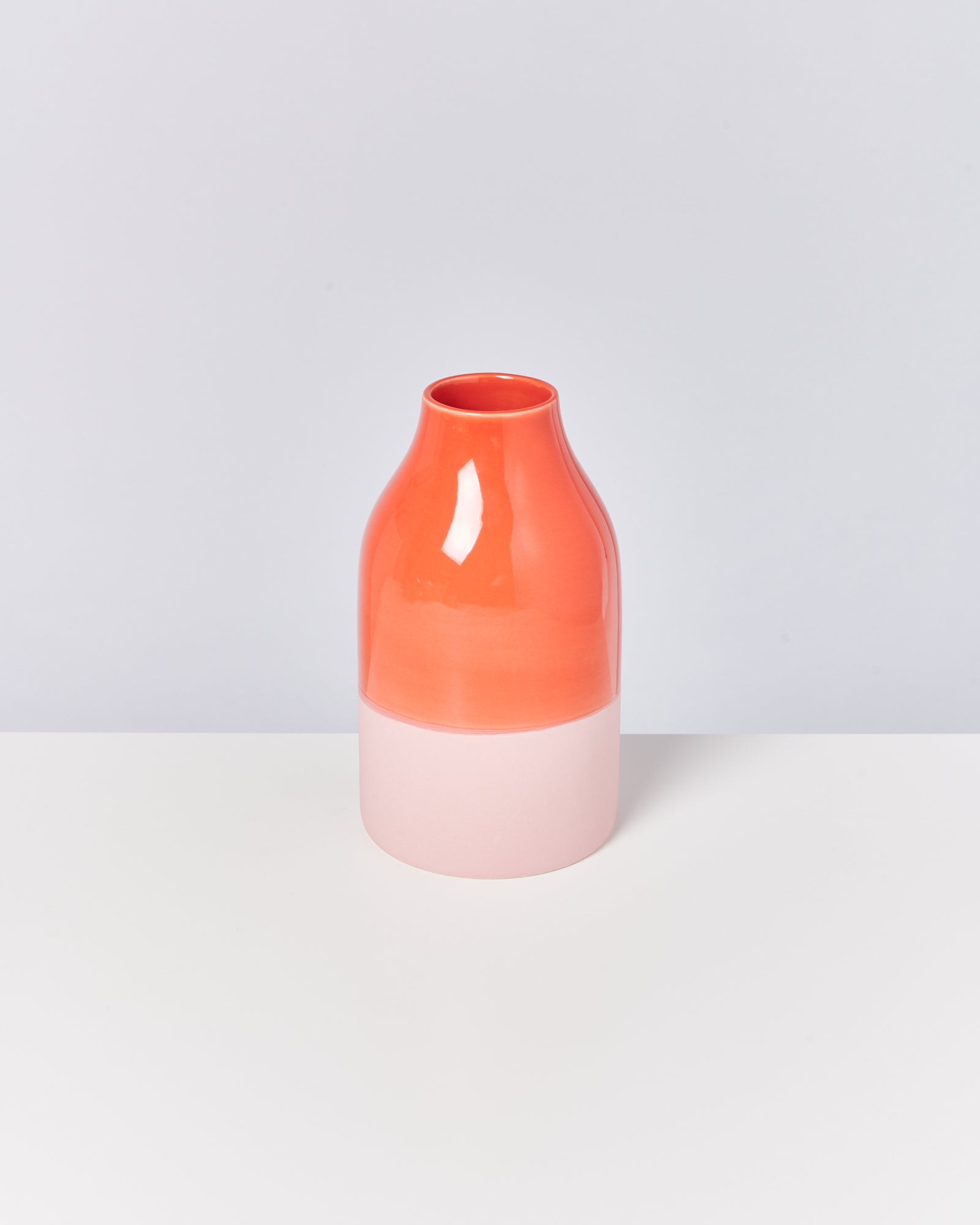 Eine zweifarbige Vase in Lachsrosa und Orange steht auf einem weißen Tisch vor einem hellgrauen Hintergrund.