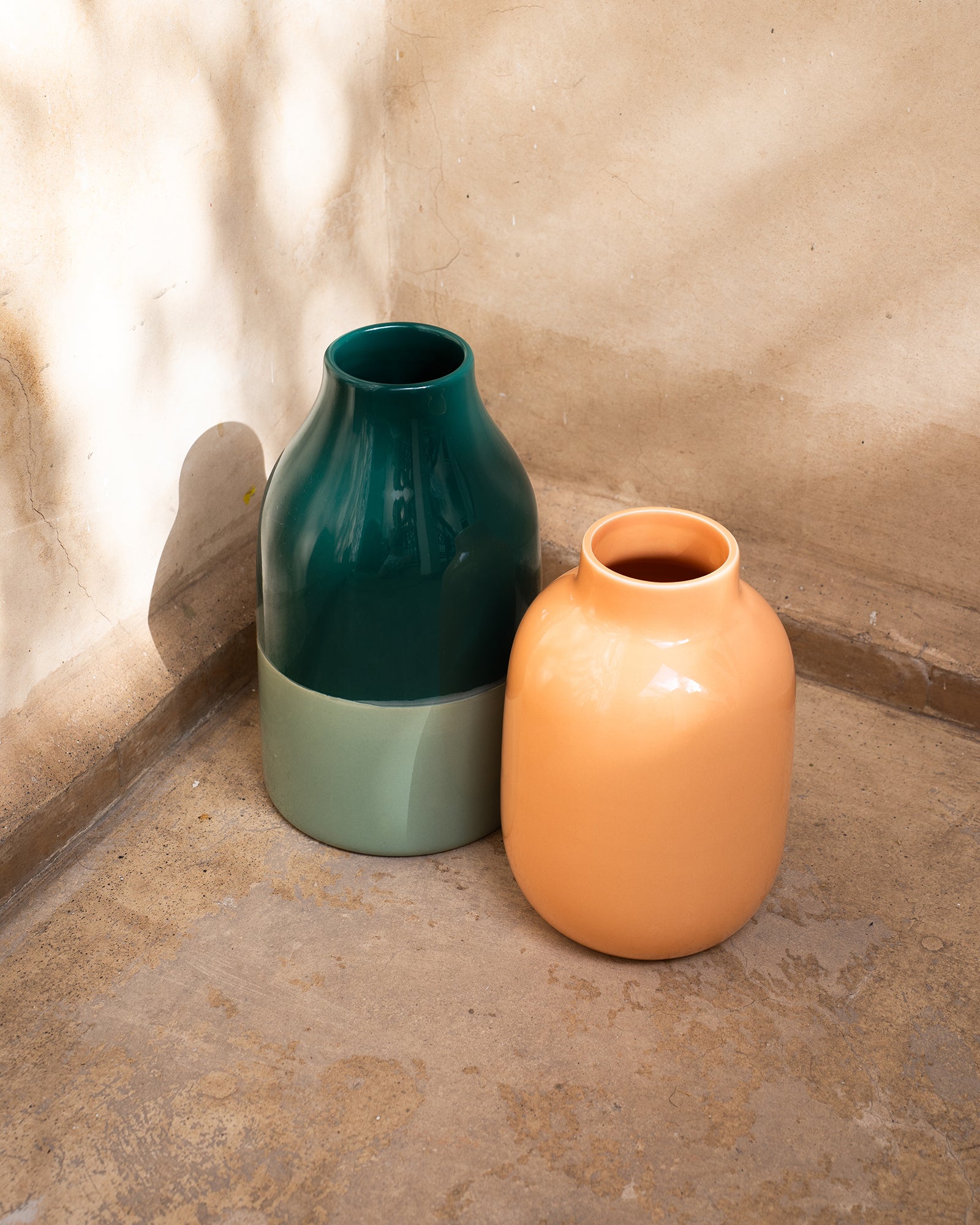 Zwei große Keramikvasen, eine in Grün und die andere in Orange, stehen auf einem Betonboden in einer Ecke.