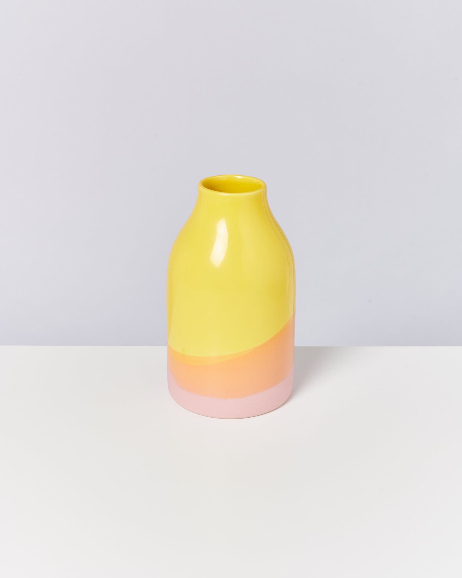 Gelbe Vase mit rosa und orangefarbenem Boden auf weißem Untergrund.
