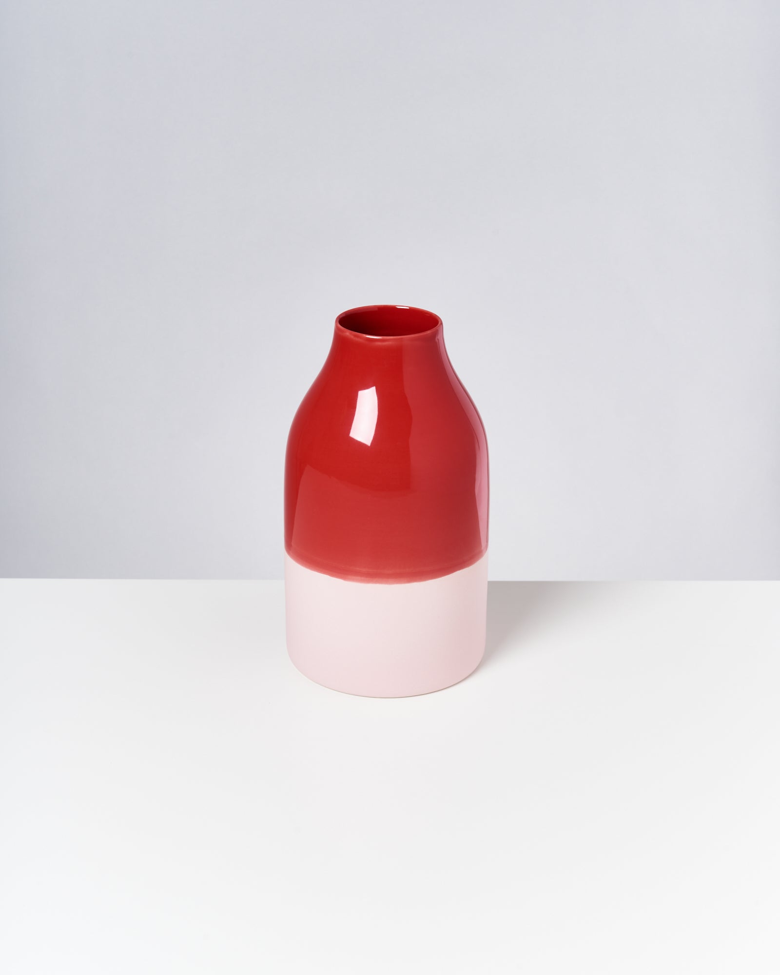 Rot-weiße Vase auf einer weißen Oberfläche vor neutralem Hintergrund.