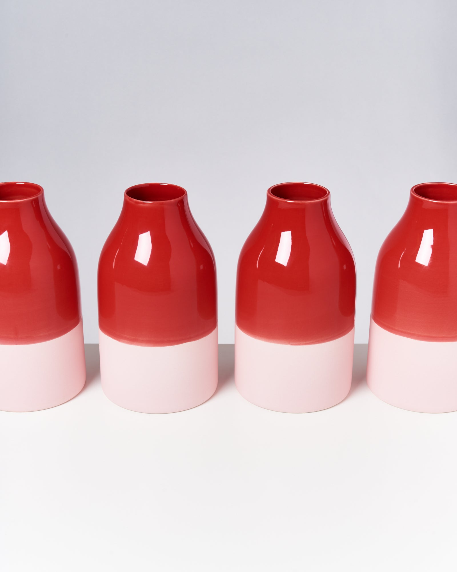 Vier rot-weiße Keramiken stehen in einer Reihe auf einer weißen Oberfläche vor einem grauen Hintergrund.