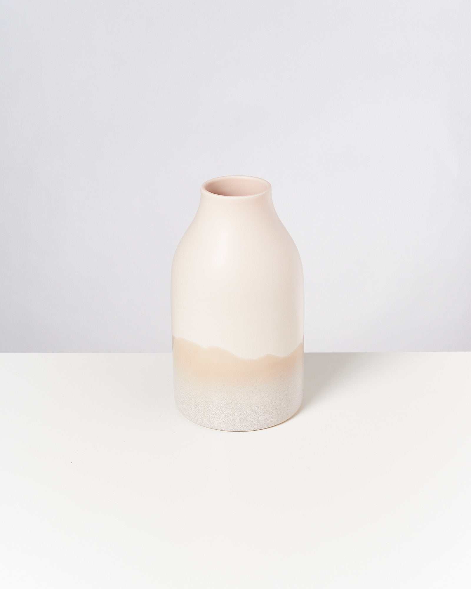 Beigefarbene, minimalistische Vase mit sanften Farbverläufen, steht auf einem weißen Untergrund vor einem hellgrauen Hintergrund.