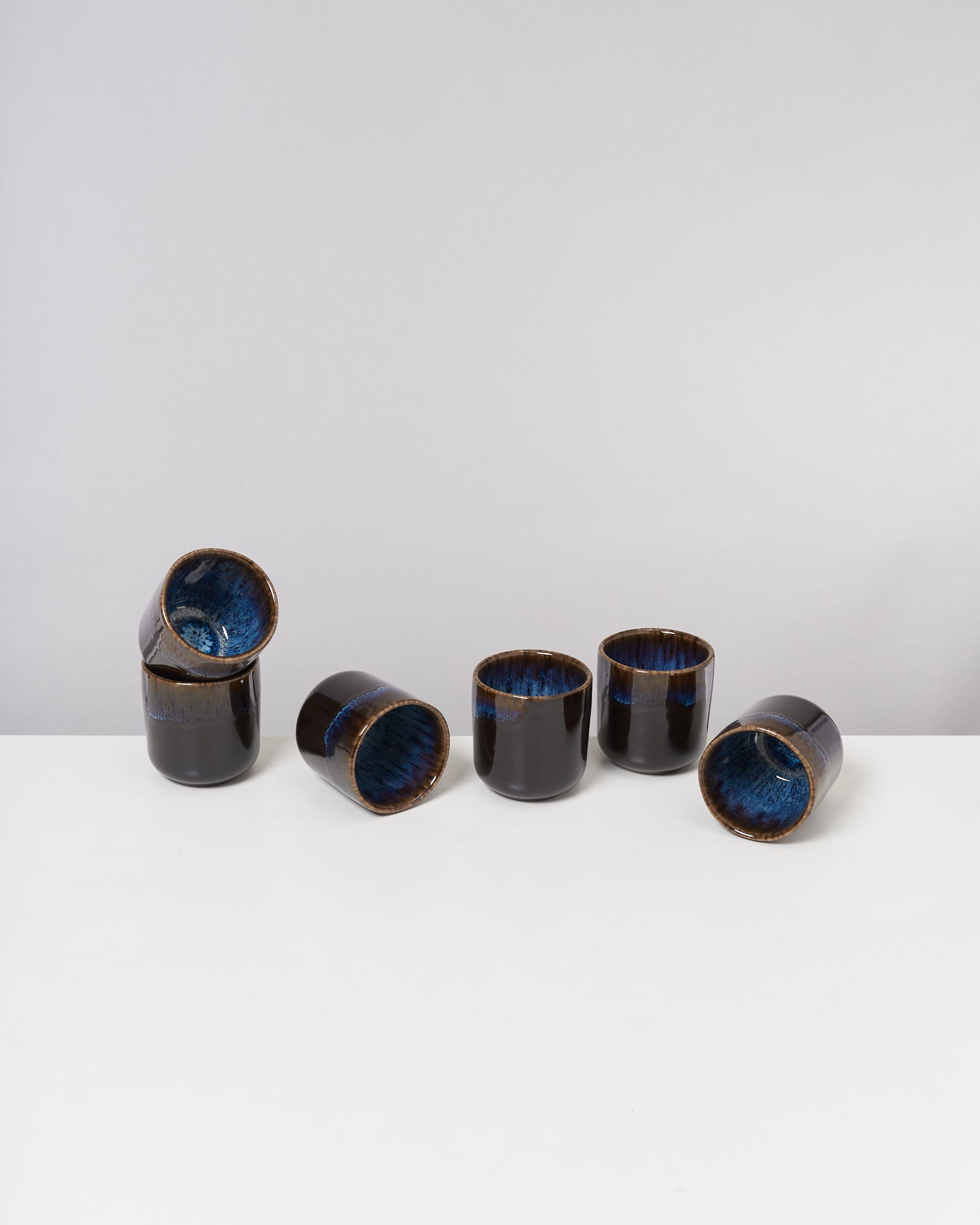 Sechs schwarz-blaue Keramikbecher auf weißem Untergrund, einige stehend und andere liegend.