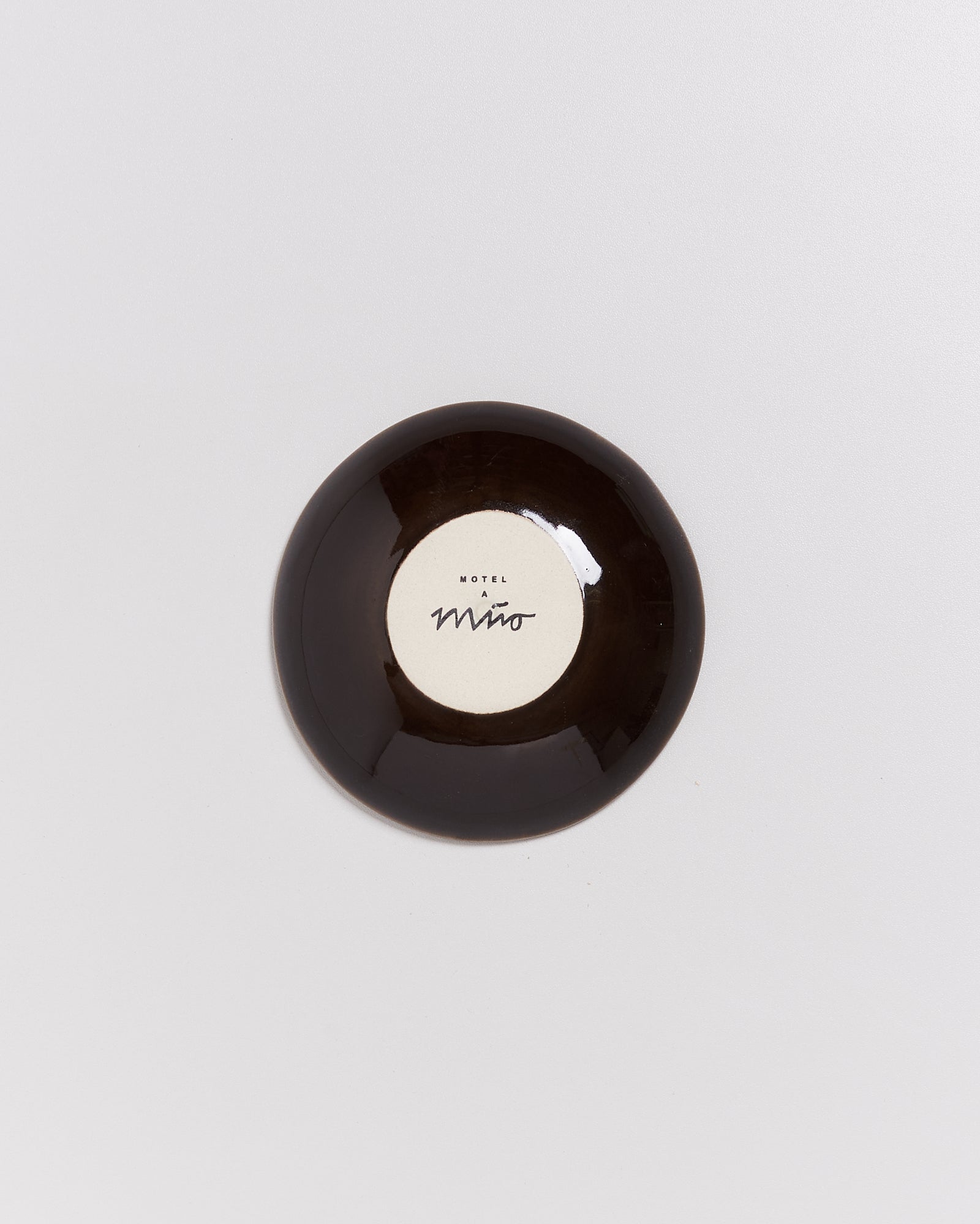 Kleine runde braune Schale mit heller Mitte und der Aufschrift "Motel a Miio" auf weißem Hintergrund.