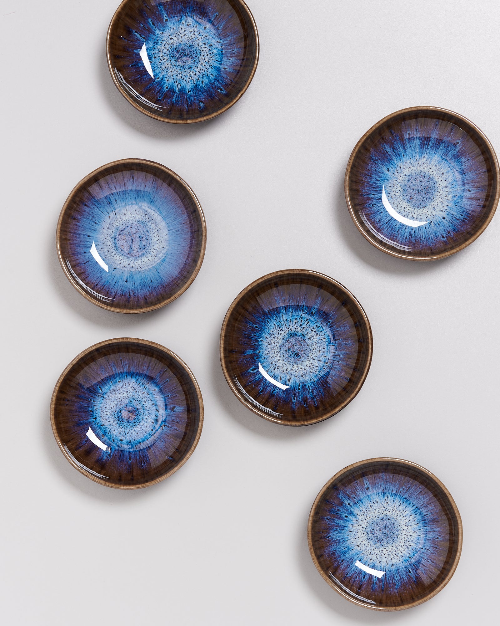 Sechs kleine Teller mit blauem, kreisförmigem Muster auf weißem Hintergrund.