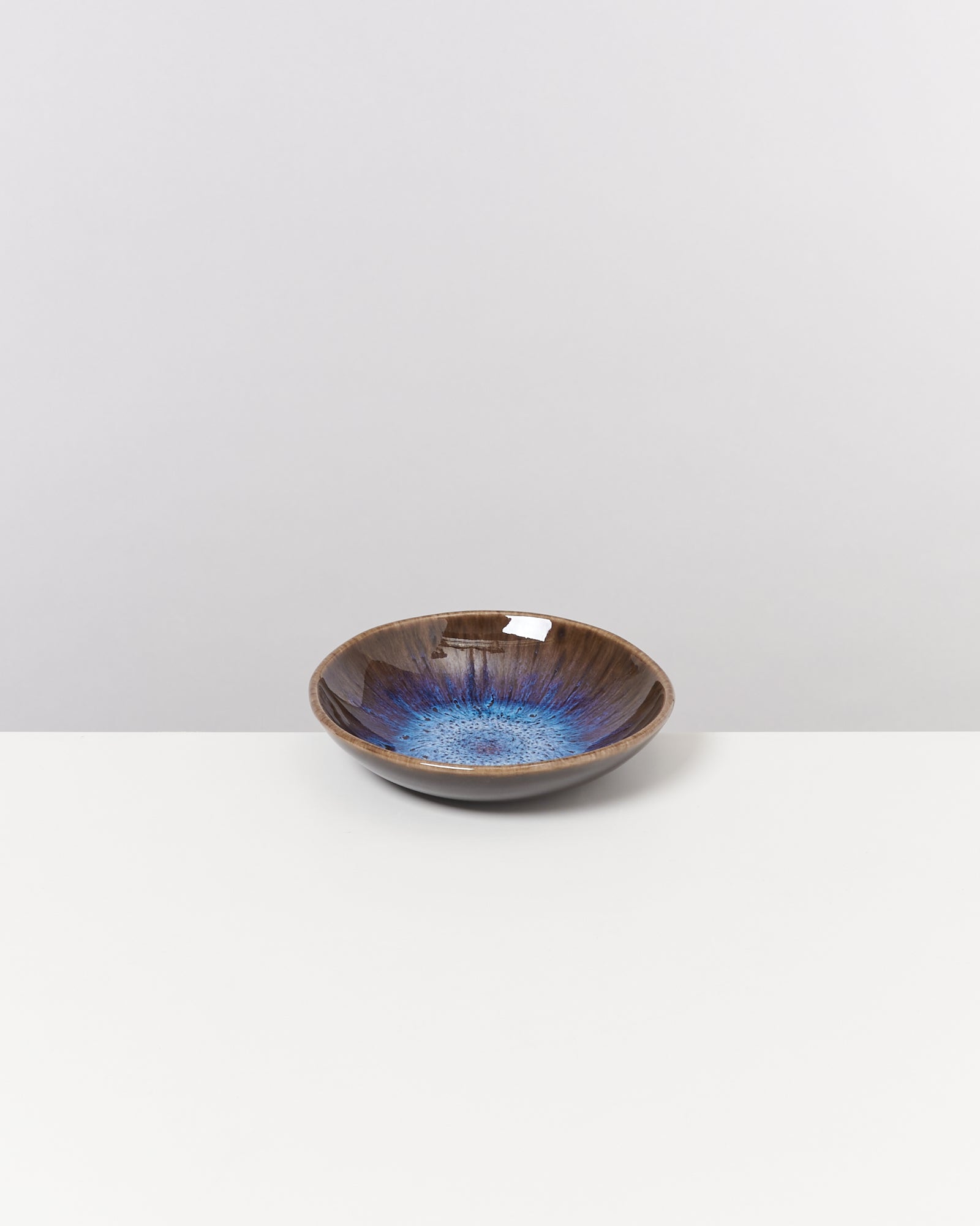 Keramikschale mit blauem Innenmuster auf weißem Tisch und grauem Hintergrund.